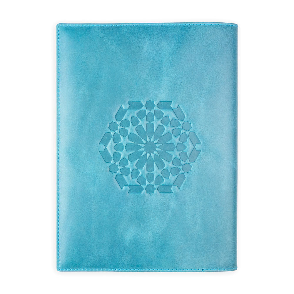 The Munira Leather Notebook Cover Zellige Blue is a handmade light blue leather cover from Spain, featuring a central embossed geometric floral design, shown against a white background.