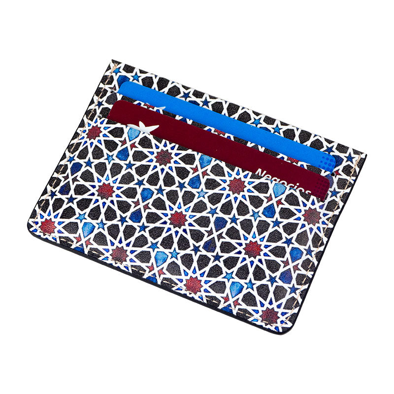 The Islamic Art Inspired Leather Cardholder Fátima Blue by Munira Leather is a handmade genuine leather accessory from Spain, with an intricate geometric design in black, white, blue, and red, holding blue and maroon cards.
