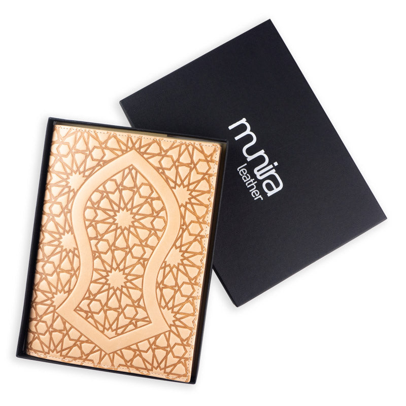 A Na´layn Leather Journal Cover Natural by Munira Leather, crafted from tan full grain leather with geometric and arabesque patterns, is shown partially out of a black Munira Leather box.