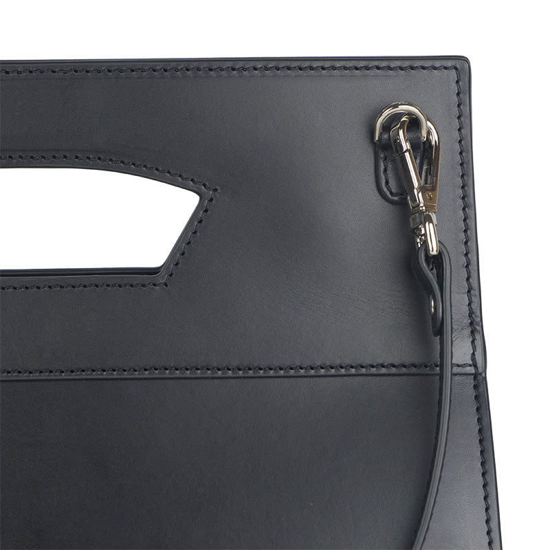 The Leather Bag Lisboa Nazarí by Munira Leather showcases black Spanish leather with sleek stitching, a rectangular cutout handle, and vegetable tanned finish. It features a metal clasp and loop for the detachable strap, presenting an elegant and minimalist design.