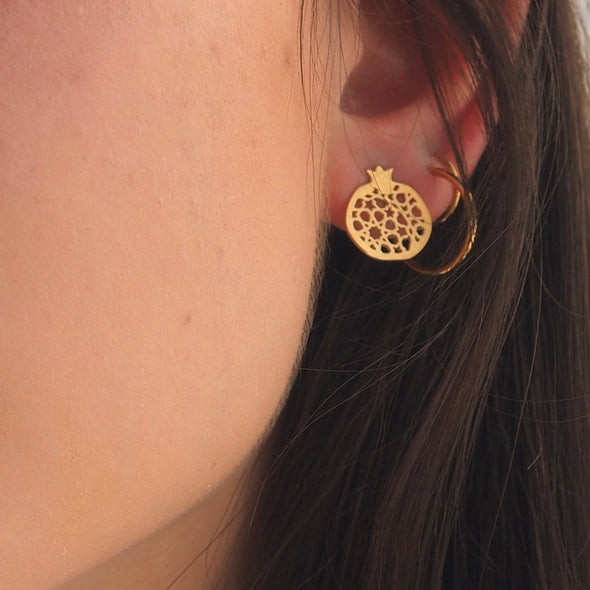 A close-up of an ear wearing Platónicas Gold Plated Stud Earrings Granada No.4 highlights the intricate cut-out details and warm tones against a softly blurred background, emphasizing the elegance of these Spanish-crafted pieces.