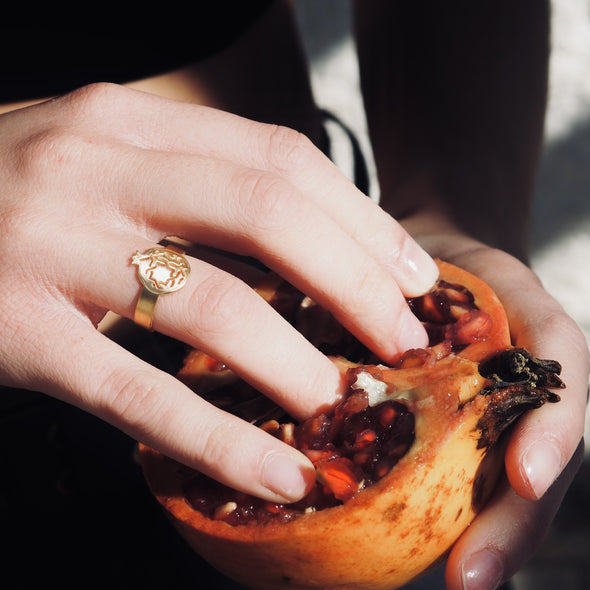 A person deftly removes seeds from a pomegranate, their fingers adorned with Platónica’s Gold Plated Thin Ring Granada No.3. Sunlight dances on the handcrafted ring, enhancing the vibrant red of the seeds and highlighting natures art alongside elegant adornment.
