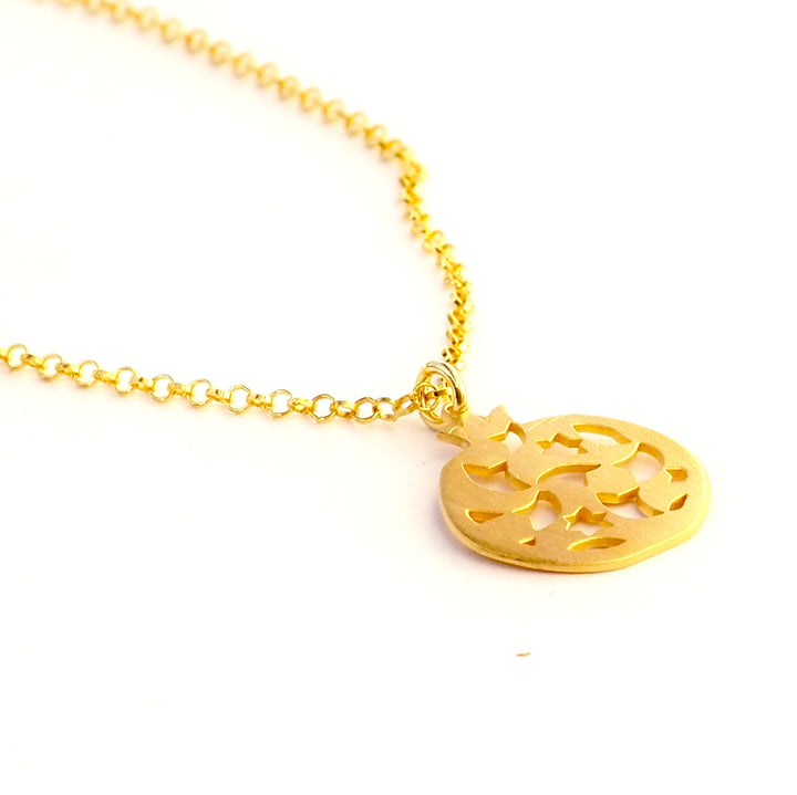 The Gold Plated Pendant Granada No.2 by Platónica is a gold-plated necklace with a round pendant featuring crescent moons and star cut-outs, elegantly lying against a white background. The chain features small round links that beautifully complement the polished pendant.