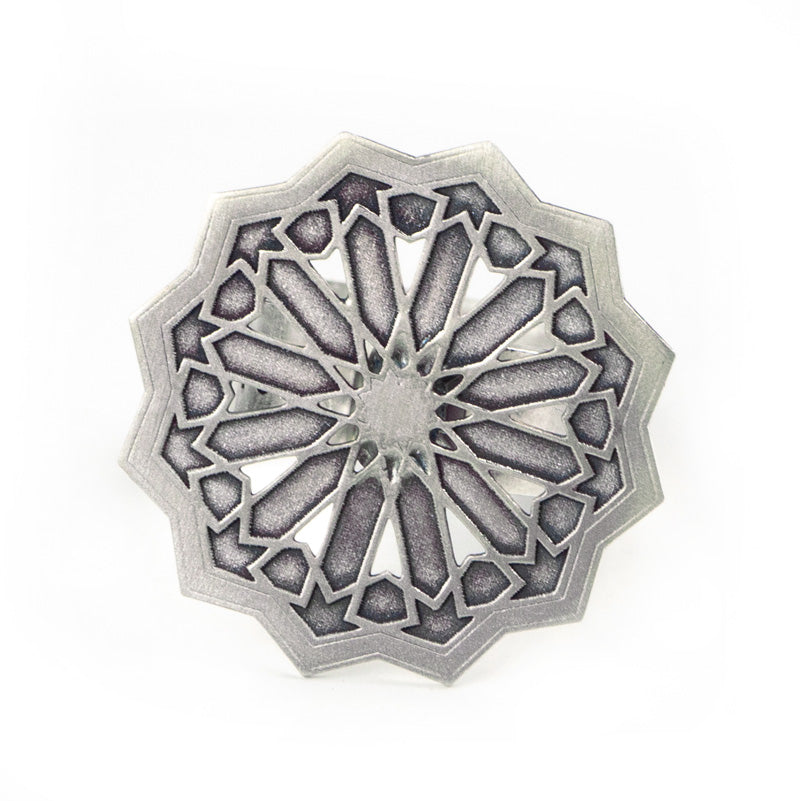 The Platónica Silver Ring Estrella Big is a handmade piece from Granada, featuring an intricate circular silver design with a geometric star-like pattern and pointed edges. Darker tones in the recessed areas enhance its textured, contemporary look.