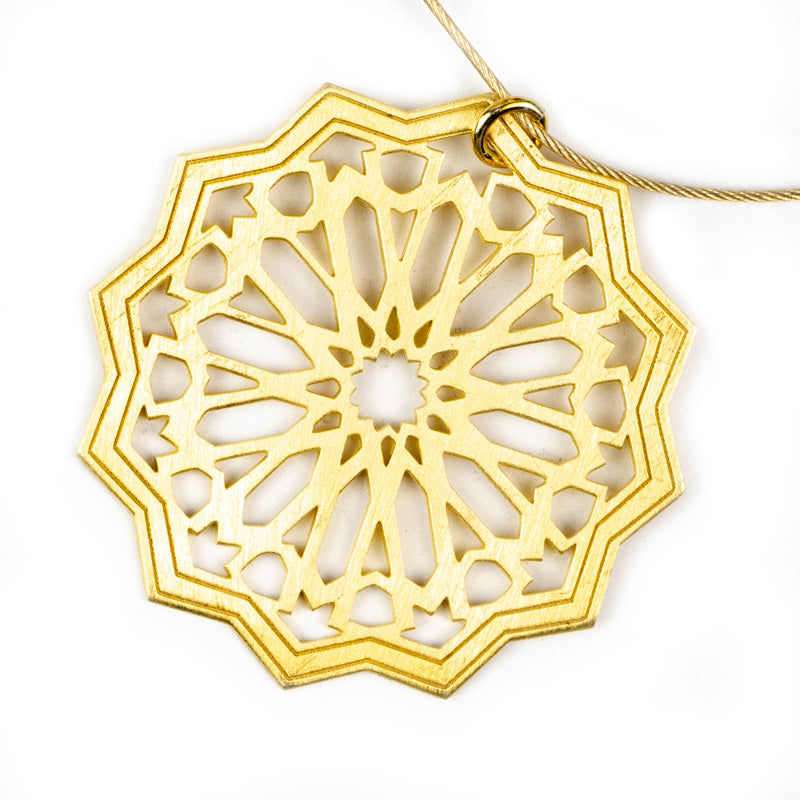 The Sterling Silver Gold Plated Pendant Estrella by Platónica features a geometric design inspired by Islamic art, with star and petal shapes in a circular pattern. Elegantly polished, it hangs gracefully from a thin chain and is exquisitely handmade in Granada.