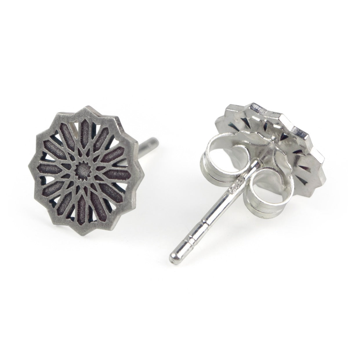 Close-up image of Platónicas Sterling Silver Studs Earrings Estrella Mini, featuring an intricate Alhambra-inspired starburst pattern with a darkened center and openwork design. Shiny earring backings enhance these stunning handmade jewels.