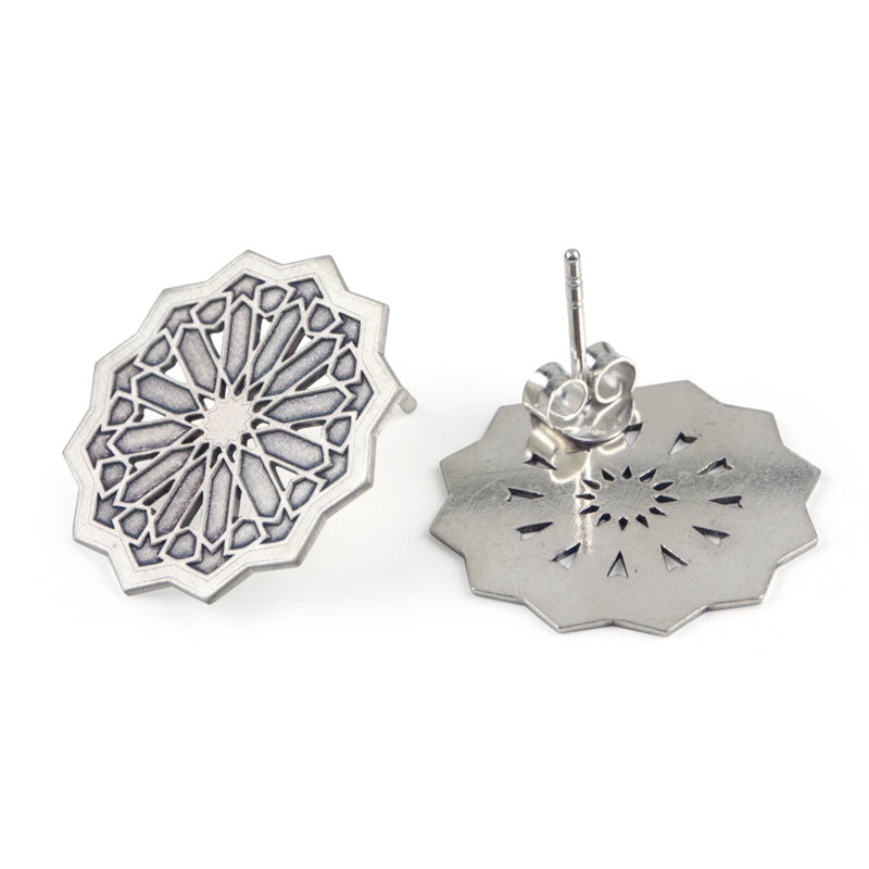 Handmade in Granada, the Platónica Sterling Silver Studs Earrings Estrella XXL feature intricate geometric patterns inspired by stained glass. These octagonal earrings boast detailed engravings and a shiny finish, with one laying flat and the other standing upright to display the back stud.