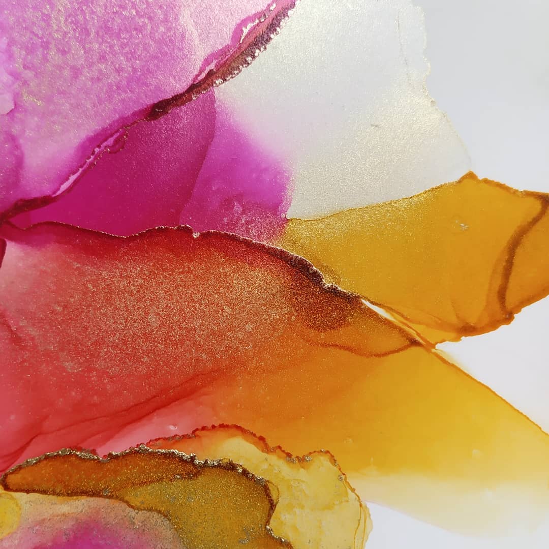 Abstract artwork featuring vibrant layers of pink, gold, orange, and yellow, with shimmering metallic accents and fluid, overlapping shapes on a white background.