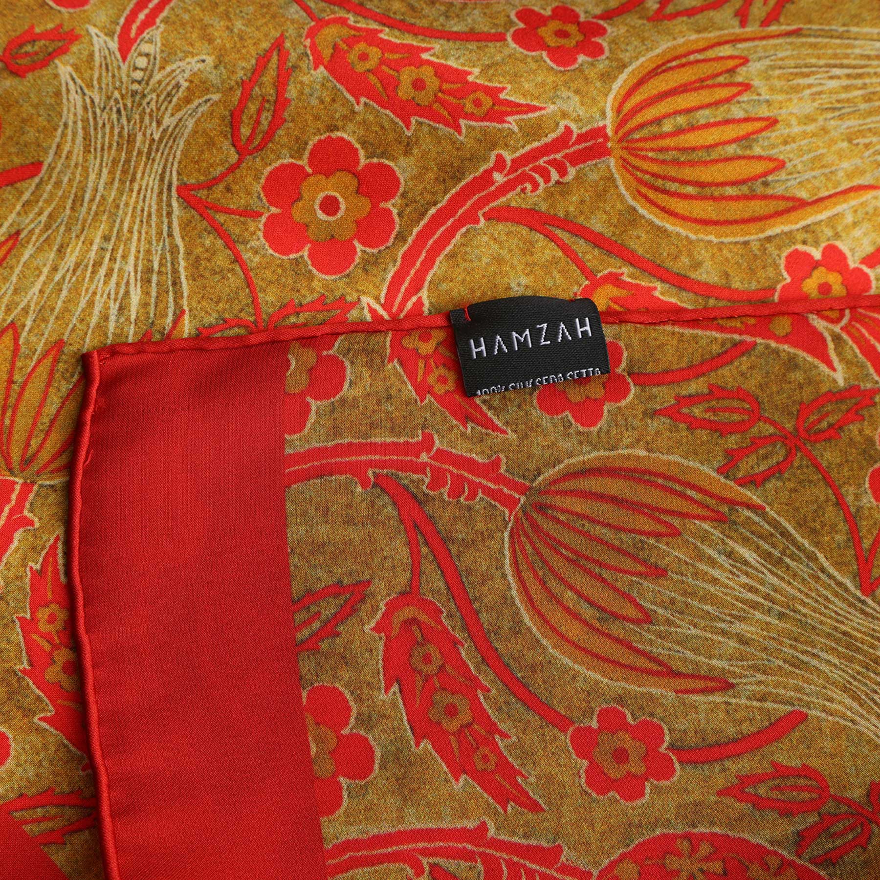 A close-up of the Floral Silk Scarf with Bold Red & Green Accents, showcasing vibrant red flowers and green leaves