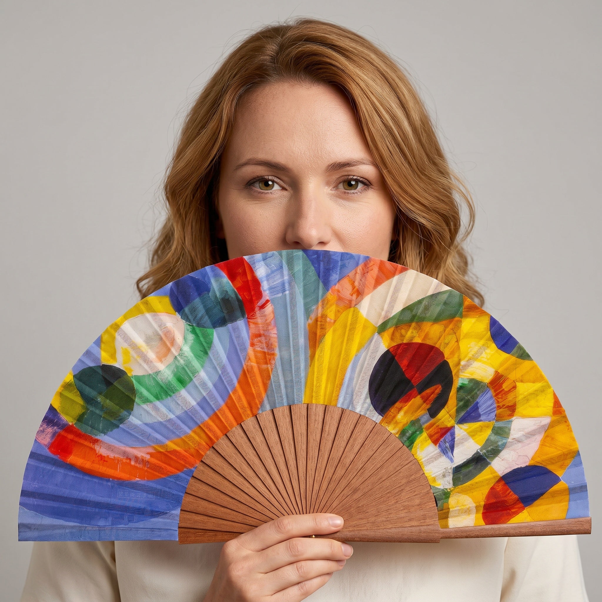 A woman holding the Robert Delaunay Print Hand Fan Elise, with its Robert Delaunay circular forms colourful print, against a soft neutral background.