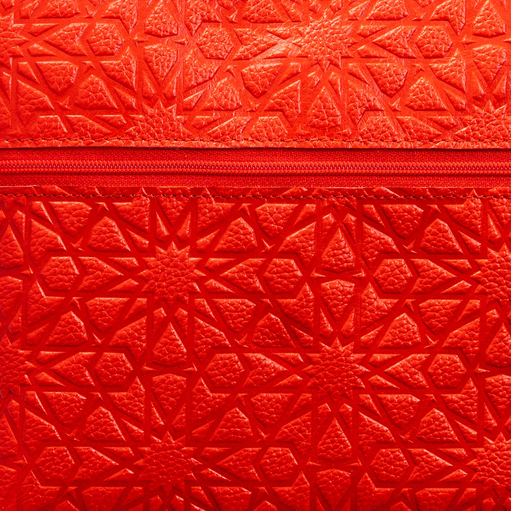 A close-up of a Red Embossed Crossbody Bag with an Islamic design pattern and a horizontal zipper across the middle.