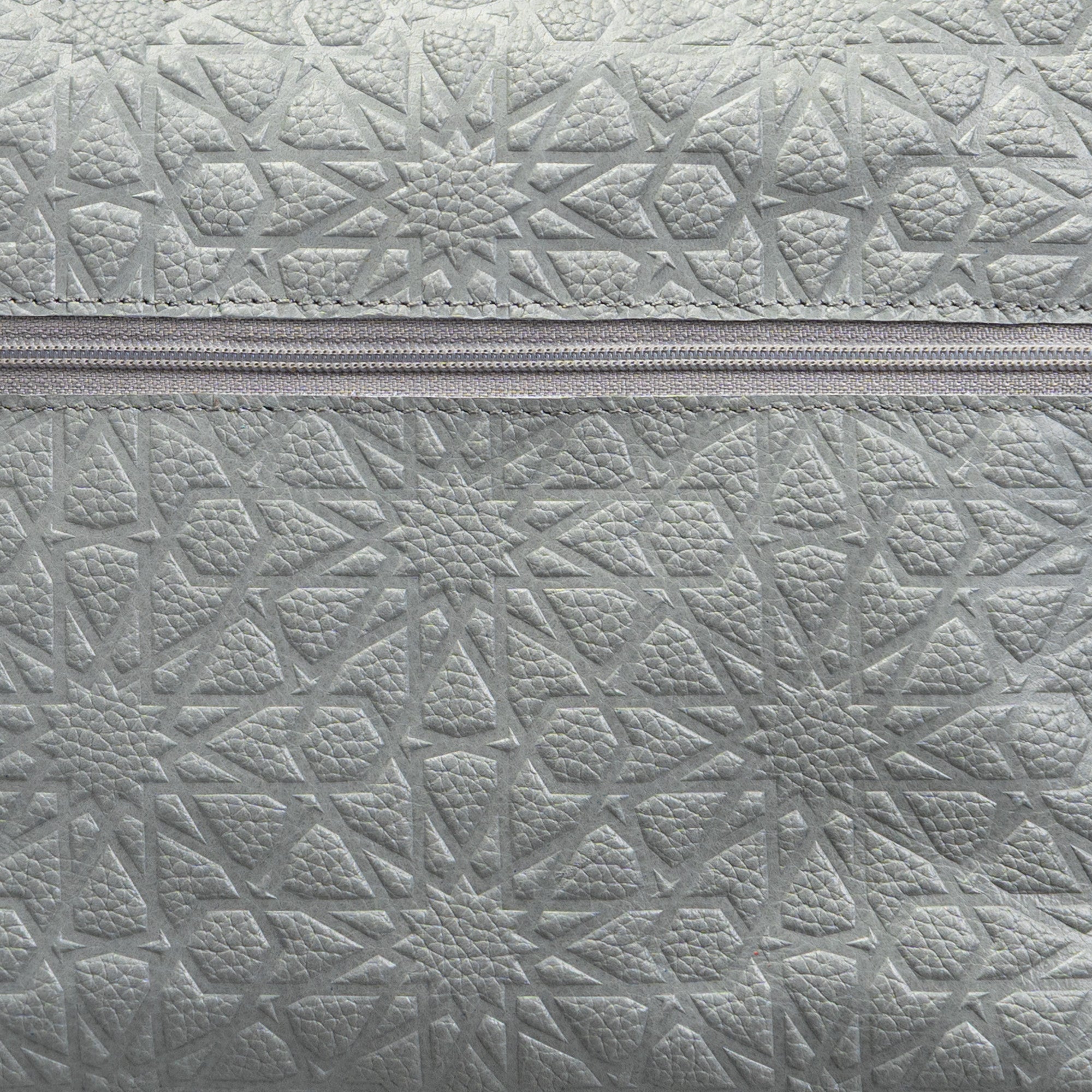 Close-up of the Gray Embossed Crossbody Bag with Islamic Design Pattern (Copia), showcasing its textured surface and a horizontal zipper across the center.