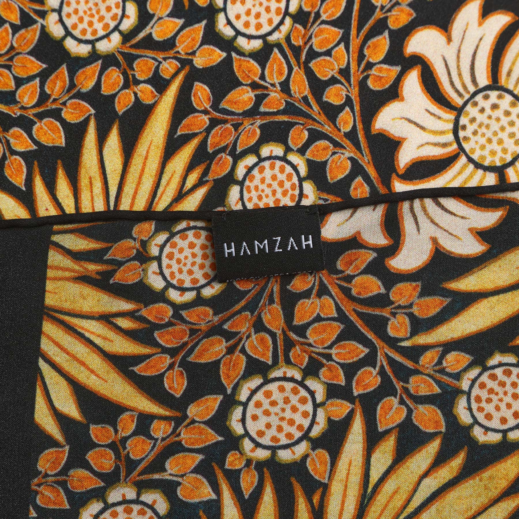 The Black Silk Scarf with Gold Floral Motifs Aurum features repeating gold floral motifs with black outlines and dark borders along the top and bottom edges.