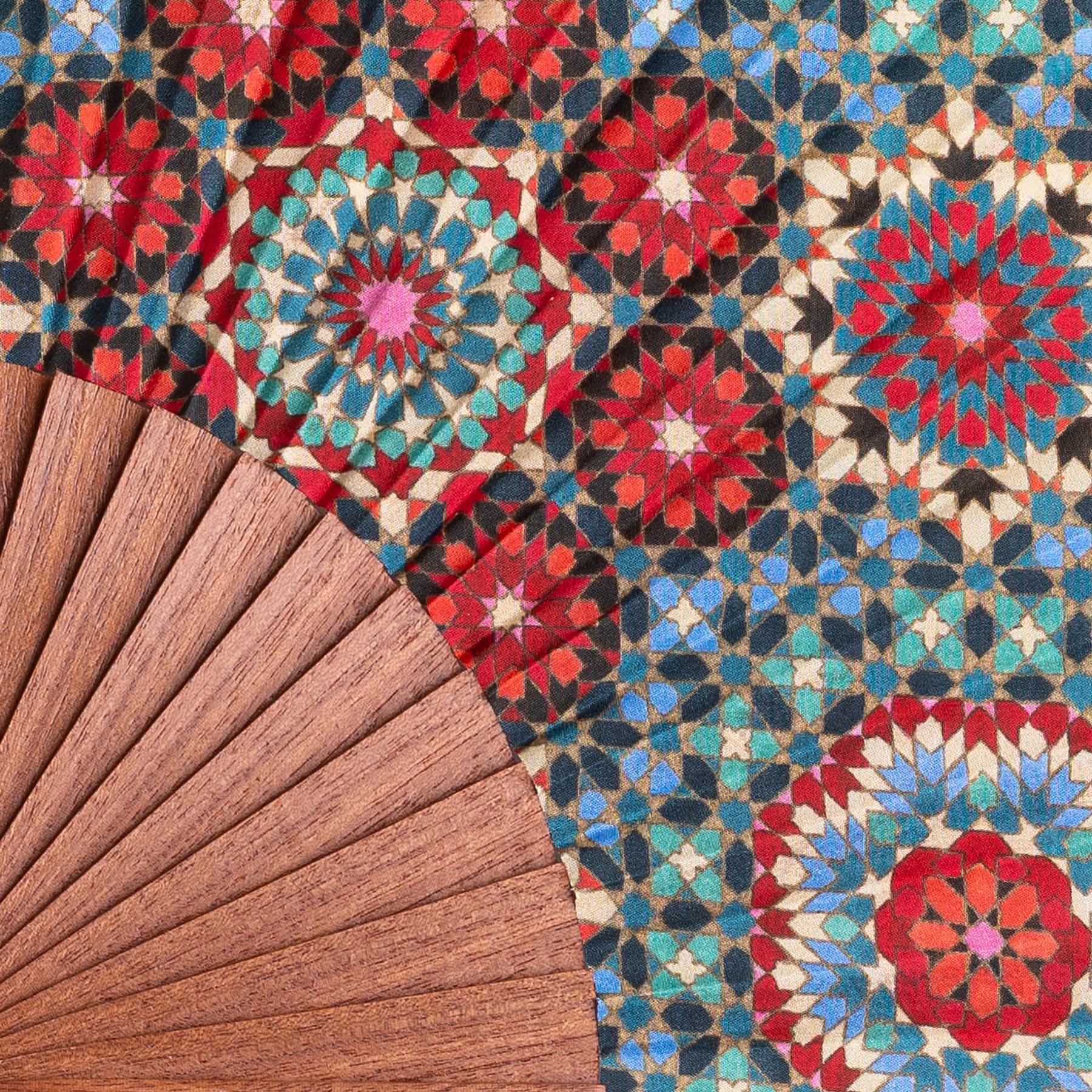 The Folding Silk Fan Baraka V1, a fine example of Spanish craftsmanship, rests on a bold mosaic surface with repeating red, blue, teal, and black geometric star patterns.