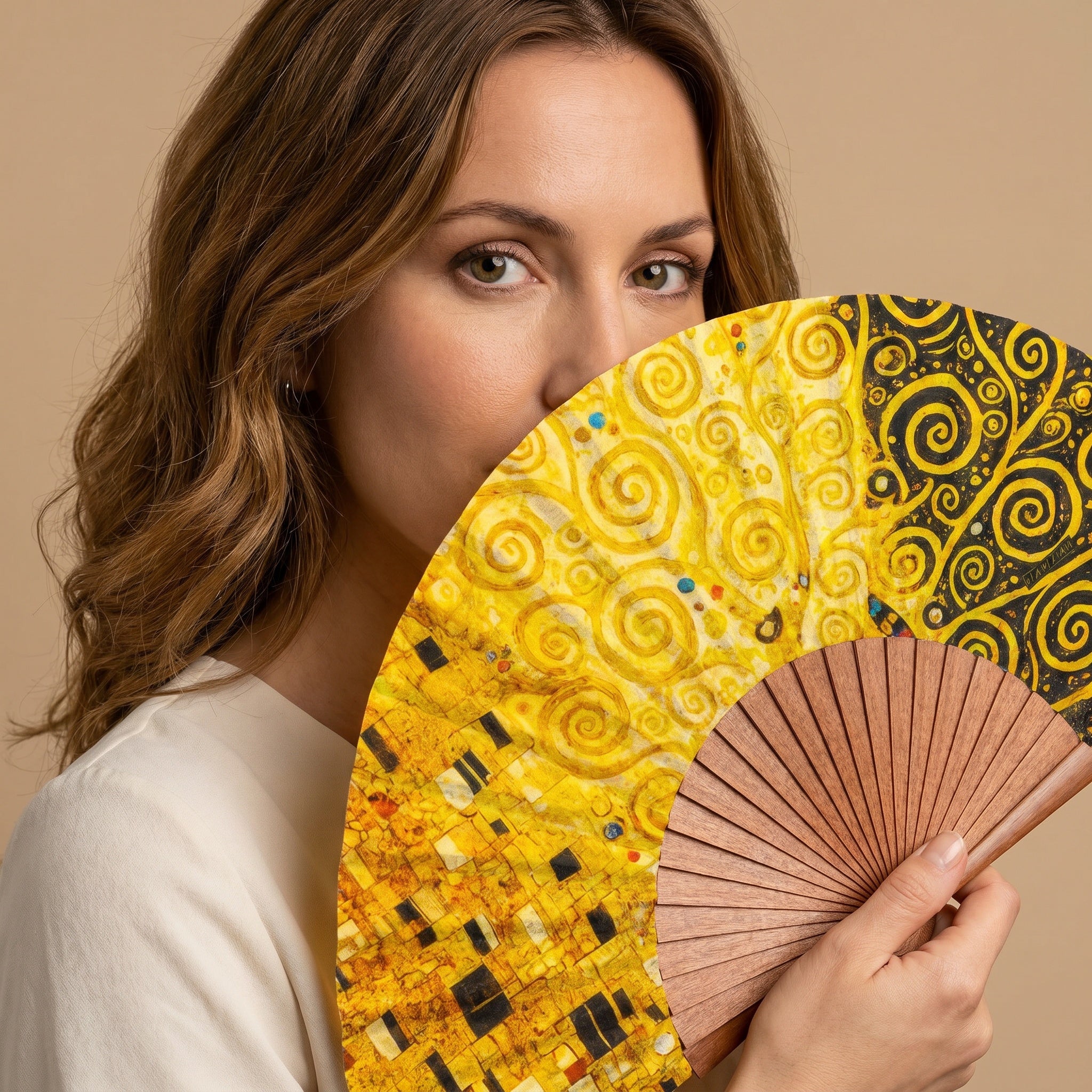 A woman holding the Gustav Klimt Print Hand Fan Tree of Life II, with its Gustav Klimt Tree of Life golden print, against a soft neutral background.