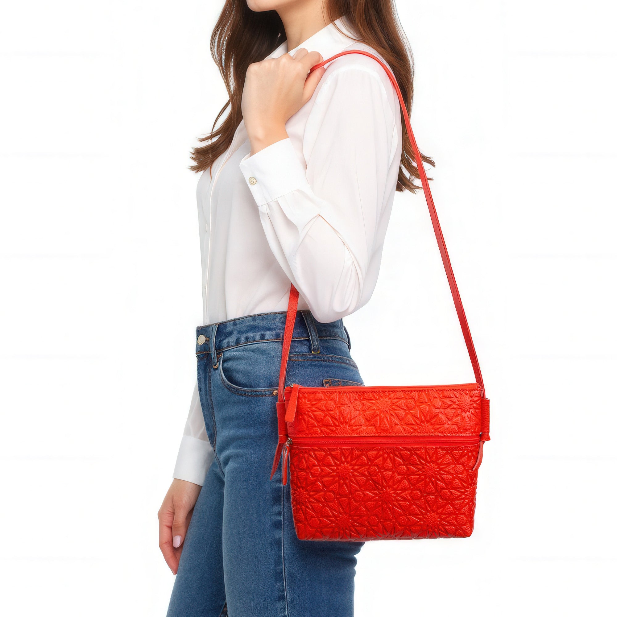 A woman in a white long-sleeve shirt and blue jeans carries the Red Embossed Crossbody Bag with Islamic Design Pattern on her shoulder. Her head is not visible in the image.