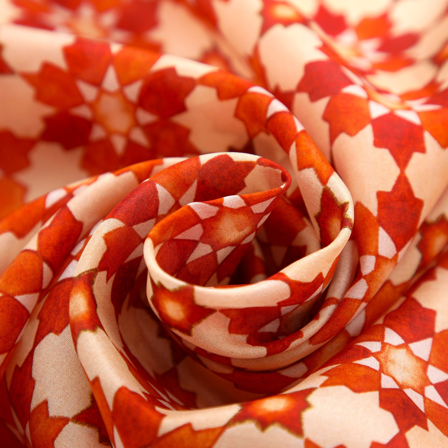 Close-up of the Orange Silk Scarf with Islamic Print Cosmo, featuring red, orange, and white geometric star patterns inspired by Andalusian art, elegantly spiraled to highlight its soft texture and depth.