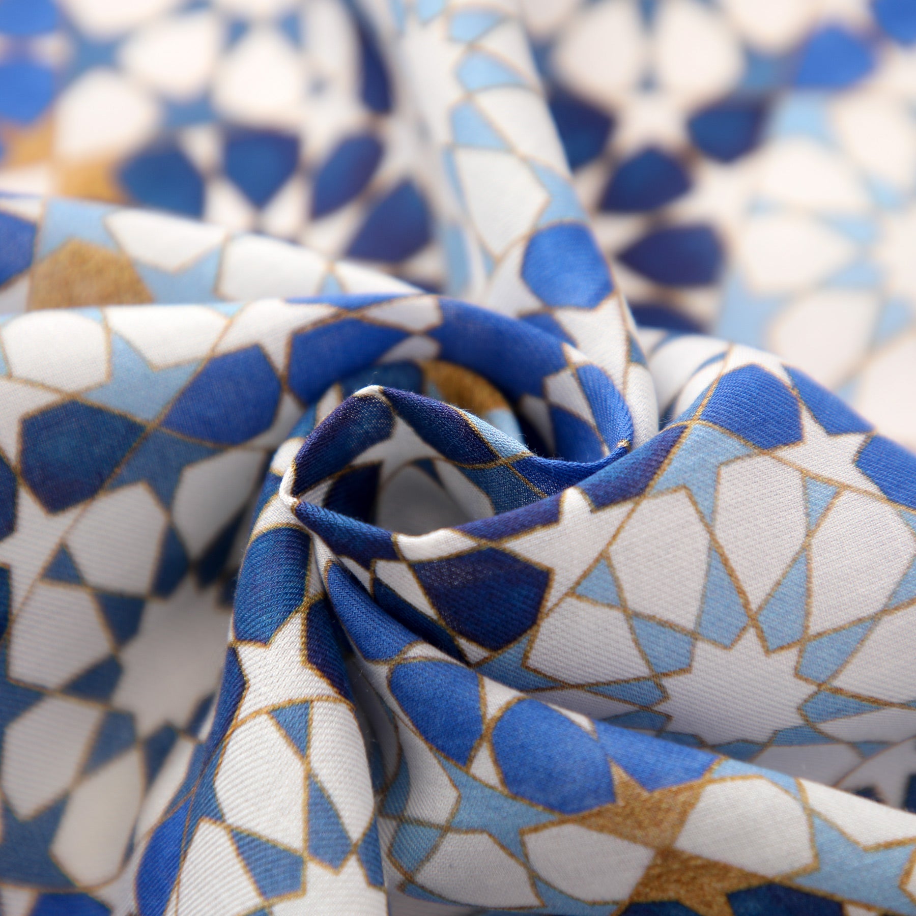 Close-up of the Blue and Gold Printed Scarf – 100% Modal, featuring an Alhambra-inspired geometric pattern in blue, white, and gold. The scarf is loosely twisted to highlight its soft folds and textured appearance.