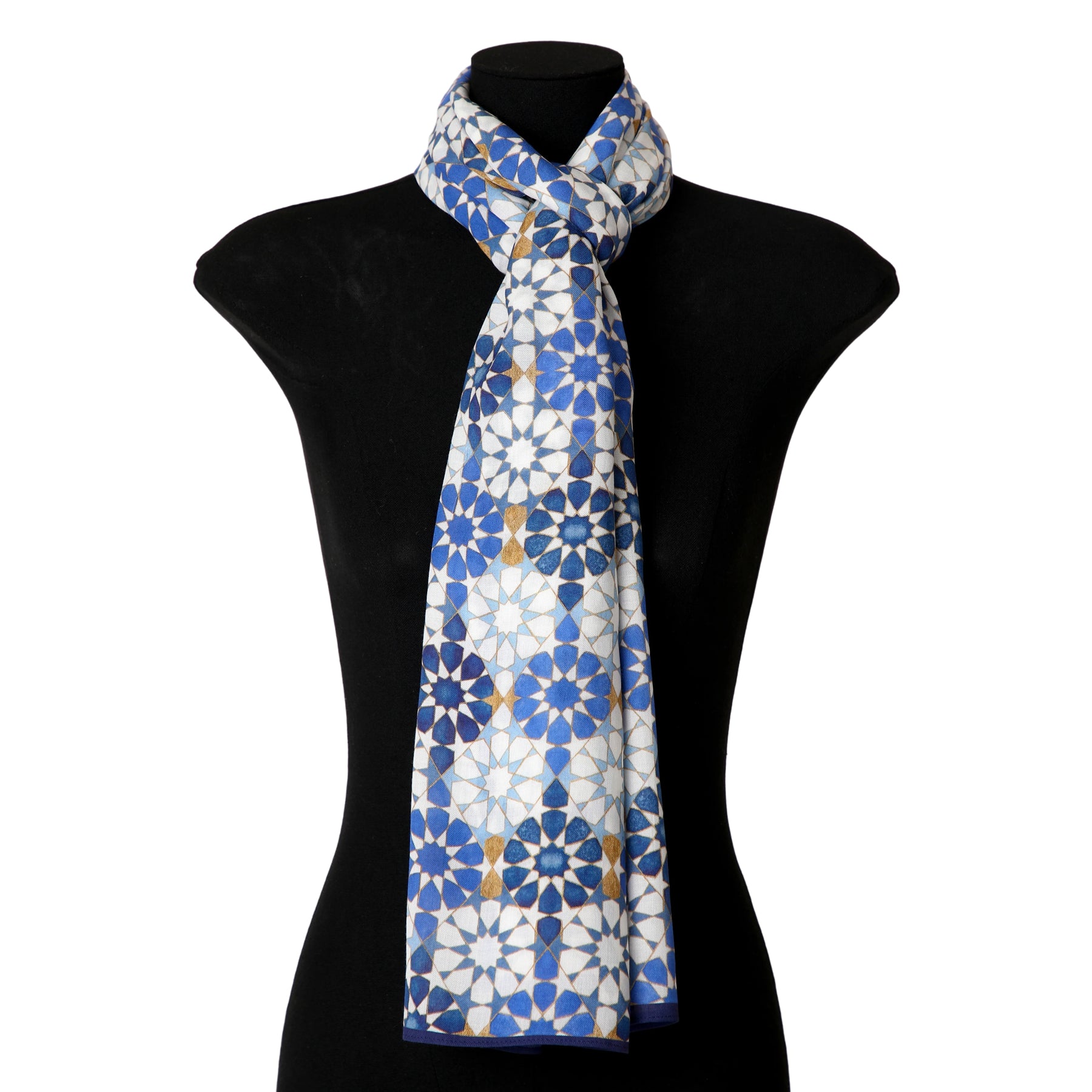 A mannequin showcases the Blue and Gold Printed Scarf—100% modal, featuring a blue, white, and gold geometric floral pattern inspired by Alhambra Islamic design—draped loosely around the neck.