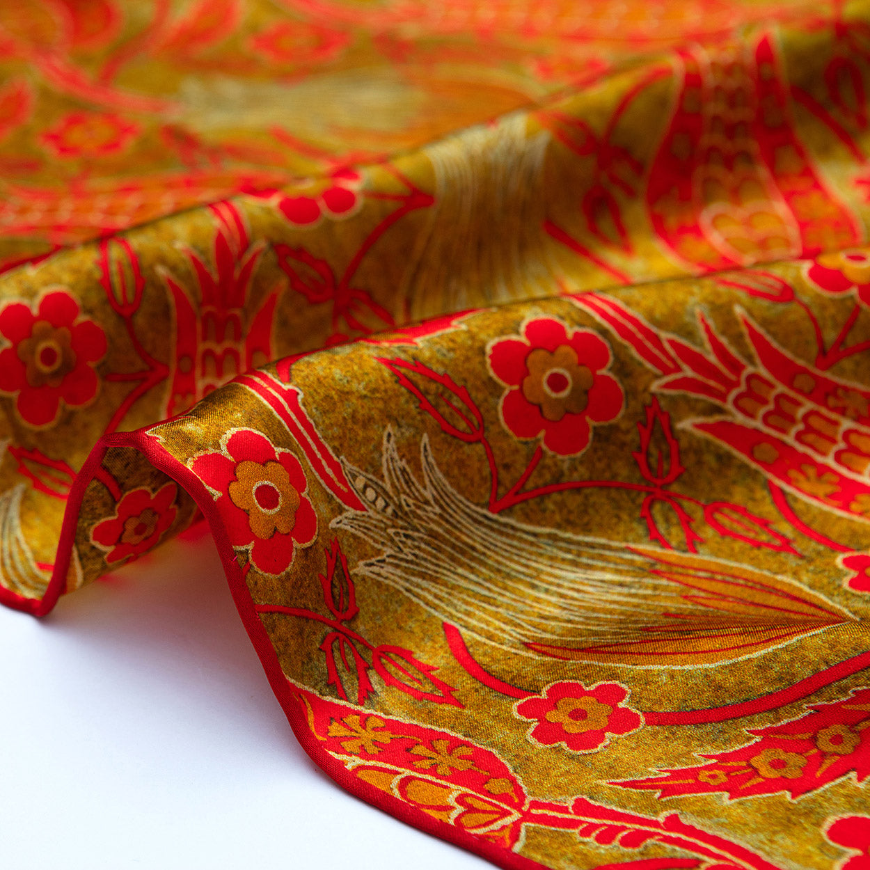 Close-up of the scarf’s hand-rolled hem, revealing vivid flower shapes against a gleaming, golden-red satin surface.