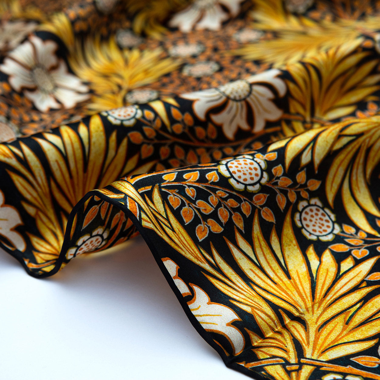 Lower edge of a black scarf decorated with bold gold leaves and subtle white blooms, emphasizing its satin finish.