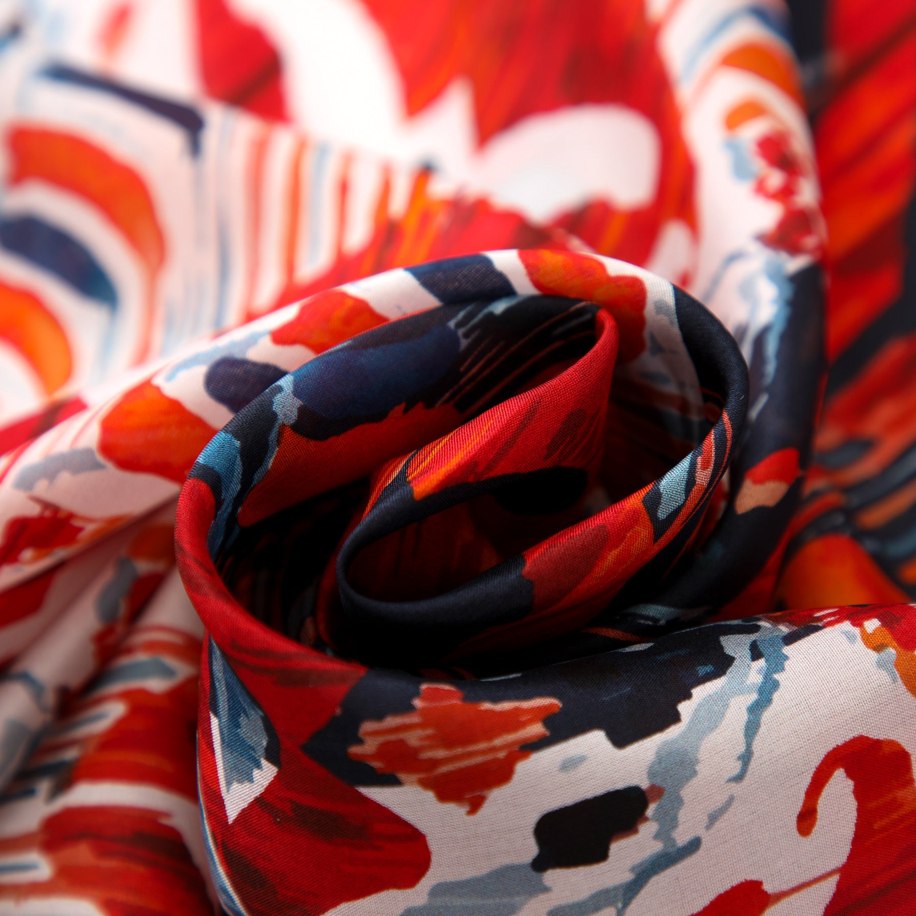 Close-up of the Red and Blue Silk Scarf with Ikat Print, featuring vibrant red, navy blue, orange, and white abstract Indonesian-inspired patterns, elegantly swirled to showcase its soft silk texture and dynamic design.