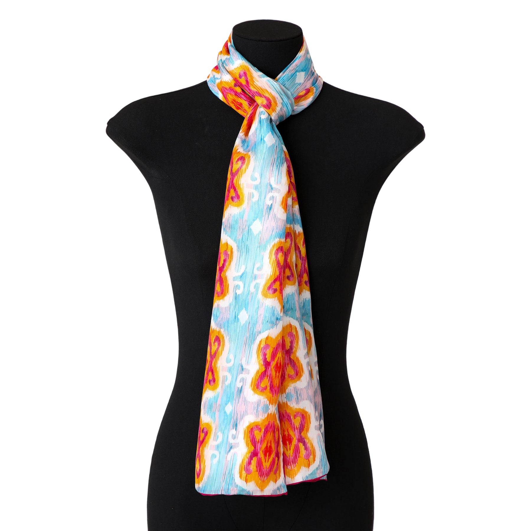 A mannequin showcases the Light Blue Silk Scarf with Ikat Print, featuring red and yellow floral patterns, elegantly draped and knotted at the neck.