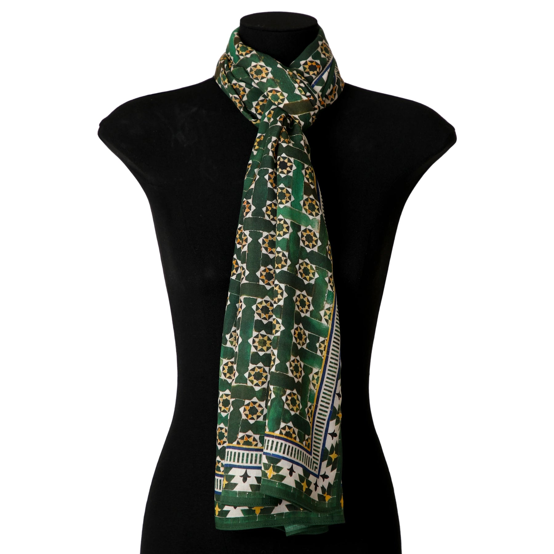The Green Modal Scarf for Women Andalusí, featuring geometric and star motifs inspired by Islamic art, is draped and knotted around the neck of a black mannequin torso.
