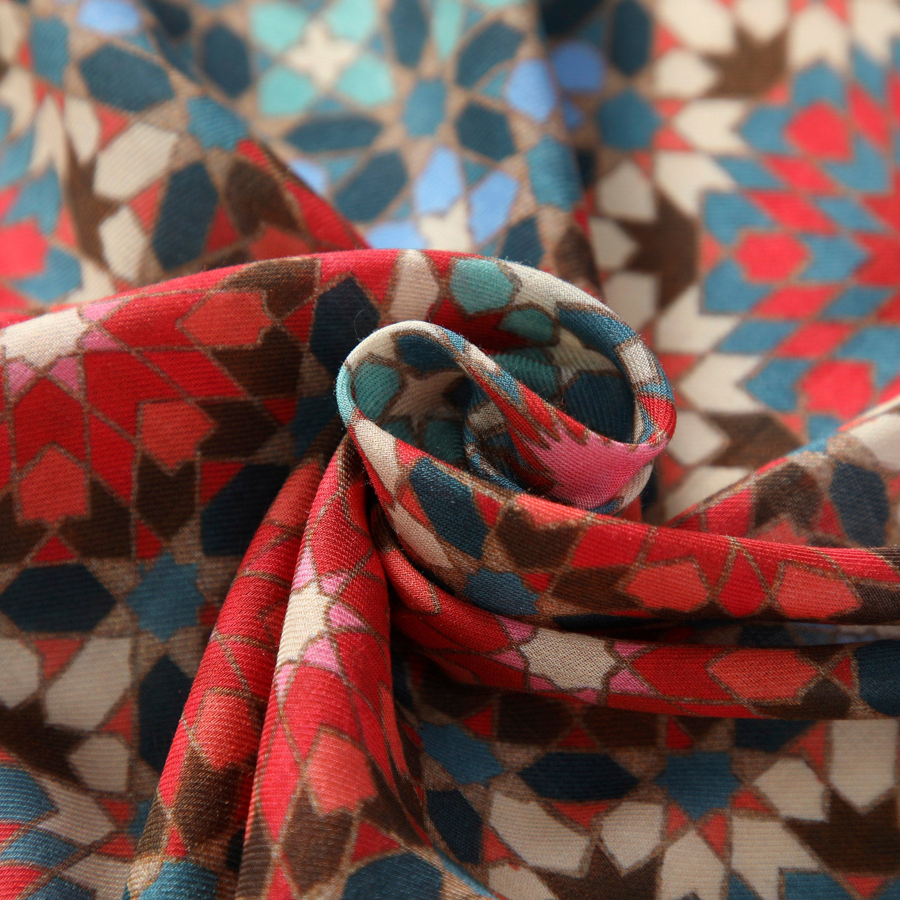 A close-up of the Multicolor Scarf Inspired by Alhambra Tiles, showcasing its geometric, kaleidoscope-like pattern in red, turquoise, brown, and blue shades, gathered into a swirl at the center.