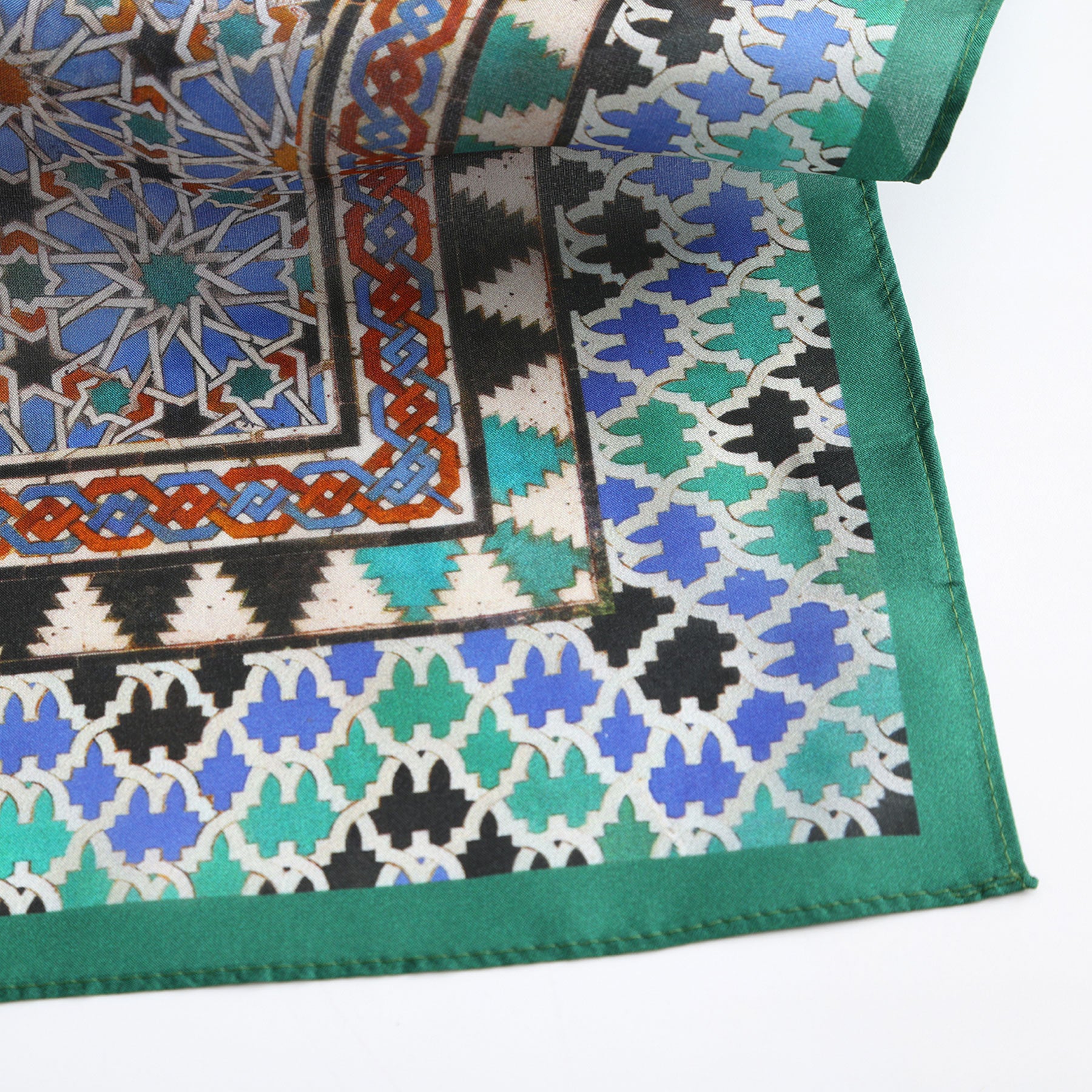A detailed view of the Alhambra Art Silk Square Scarf, showcasing an intricate green, blue, black, and white geometric mosaic with a solid green border—reflecting traditional Moorish art and Spanish craftsmanship.