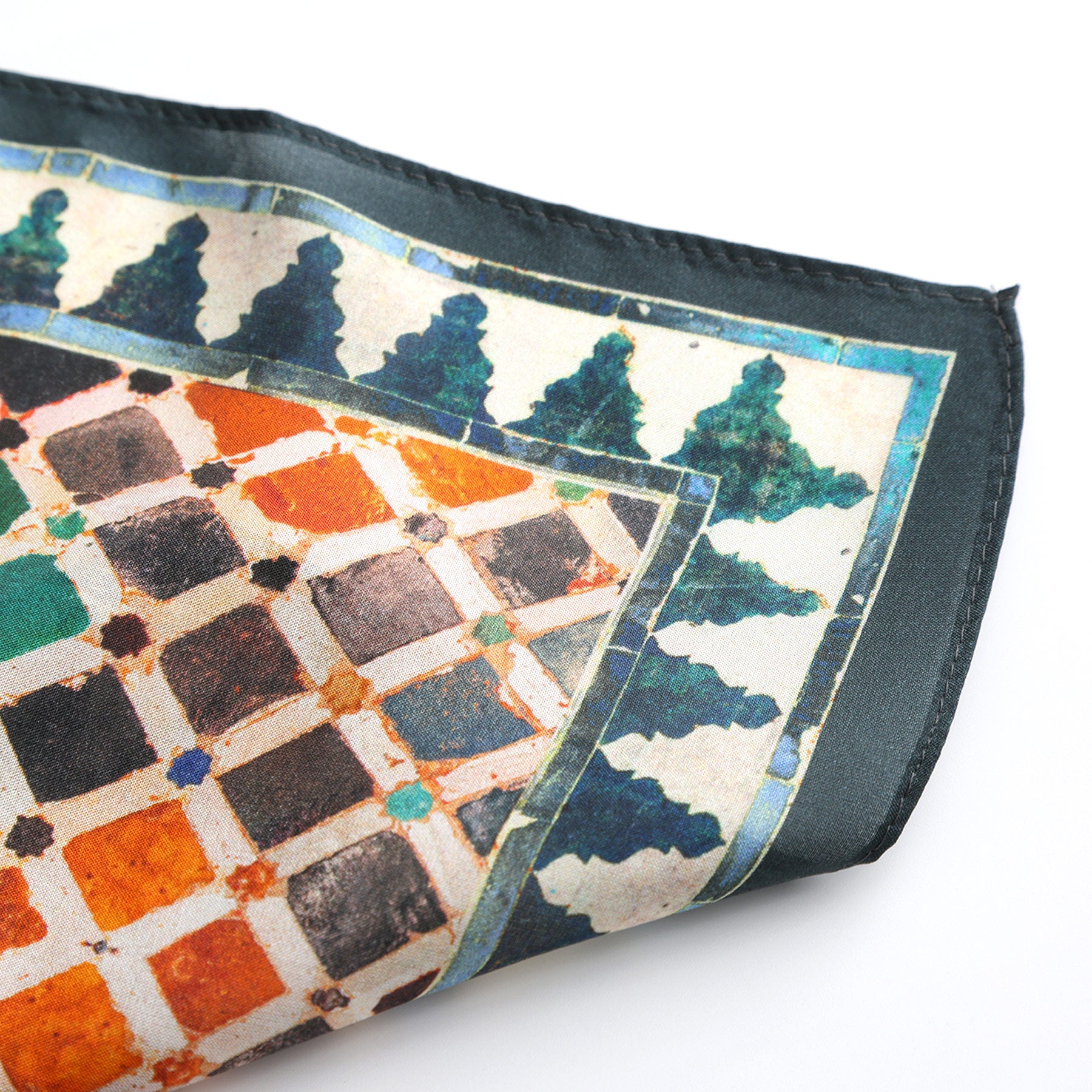 A close-up of the Colorful Square Scarf Comares, folded to reveal its geometric Alhambra print in orange, brown, and black squares with a white background and a green tree-like border.