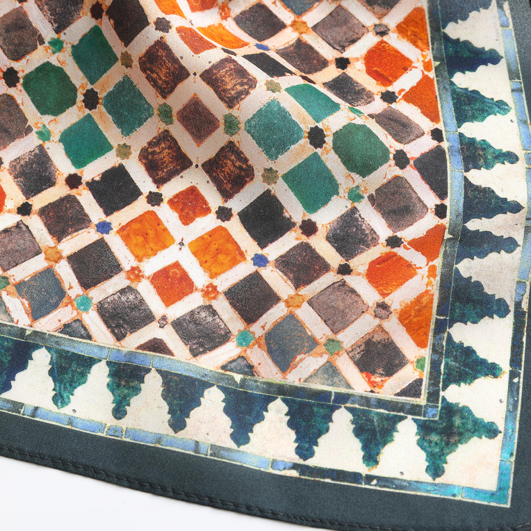 A close-up of the Colorful Square Scarf Comares, showcasing a geometric tile pattern in green, orange, black, and cream with a decorative green and blue Alhambra-inspired border.