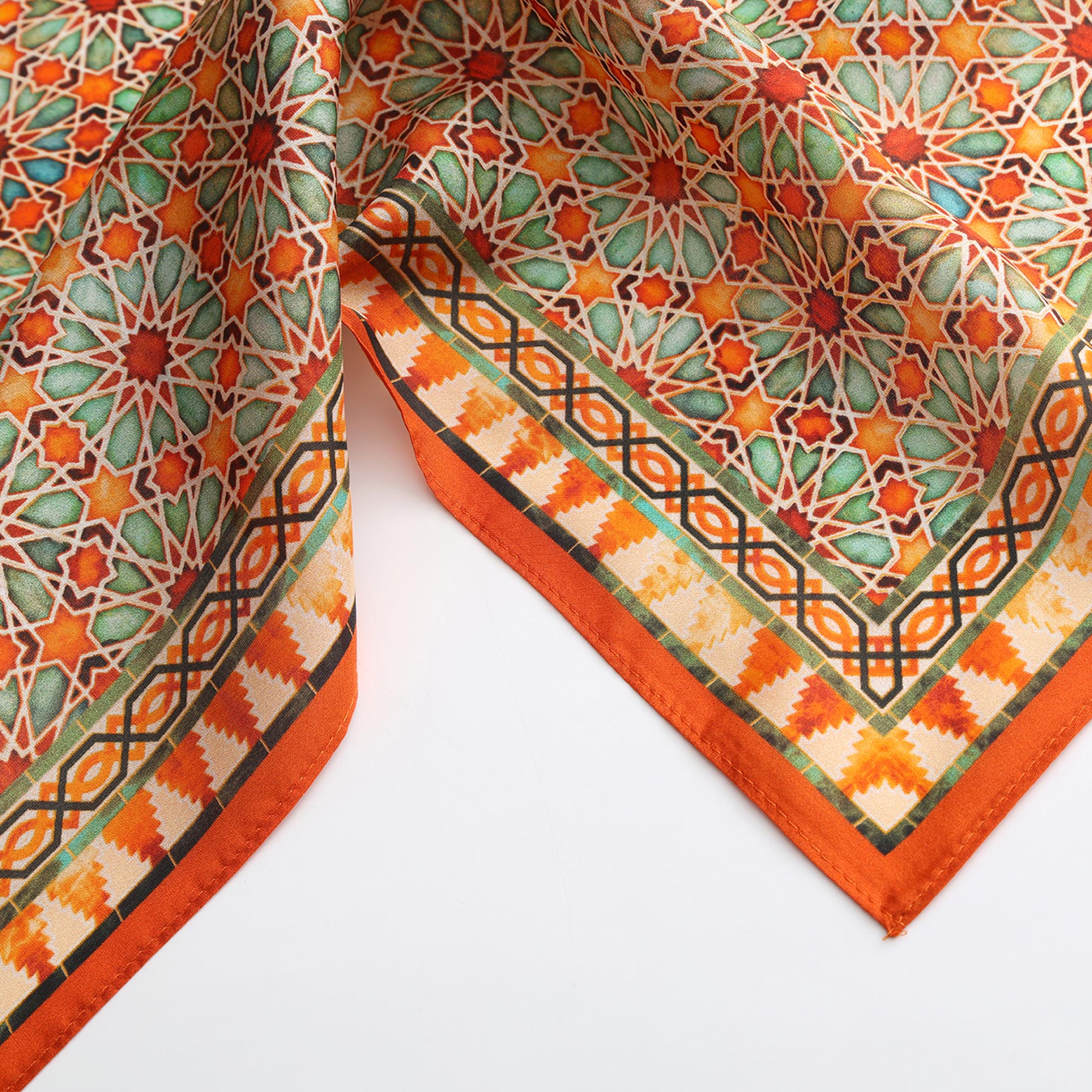 A close-up of the Orange Square Scarf Zellige shows intricate geometric designs in orange, green, yellow, and white, inspired by Islamic art motifs and decorative borders on a crisp white background.