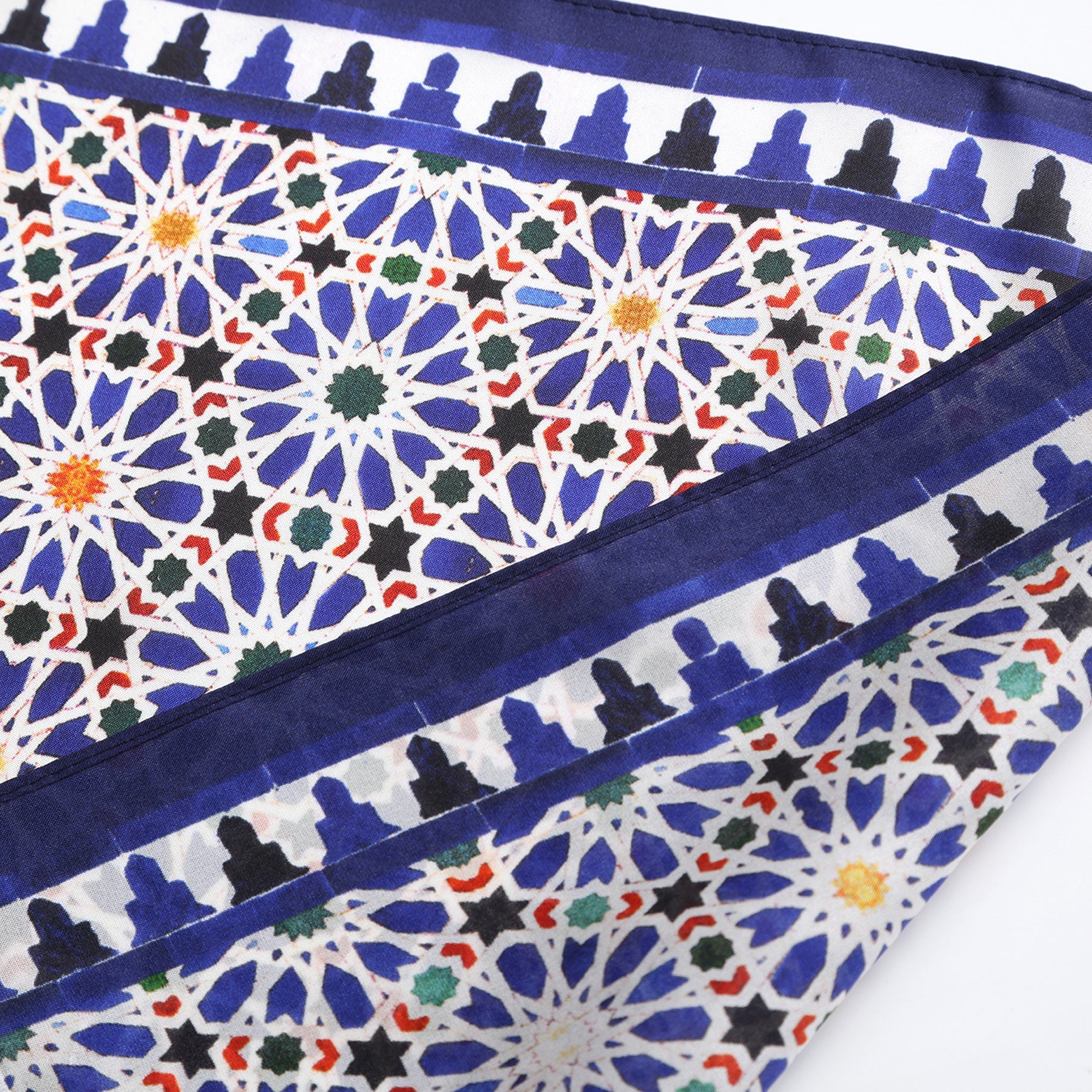 The Blue Square Scarf Zellige v2 features intricate geometric patterns in vibrant hues and a blue border with a repeating silhouette motif, inspired by traditional Islamic art and crafted with refined Spanish artistry.