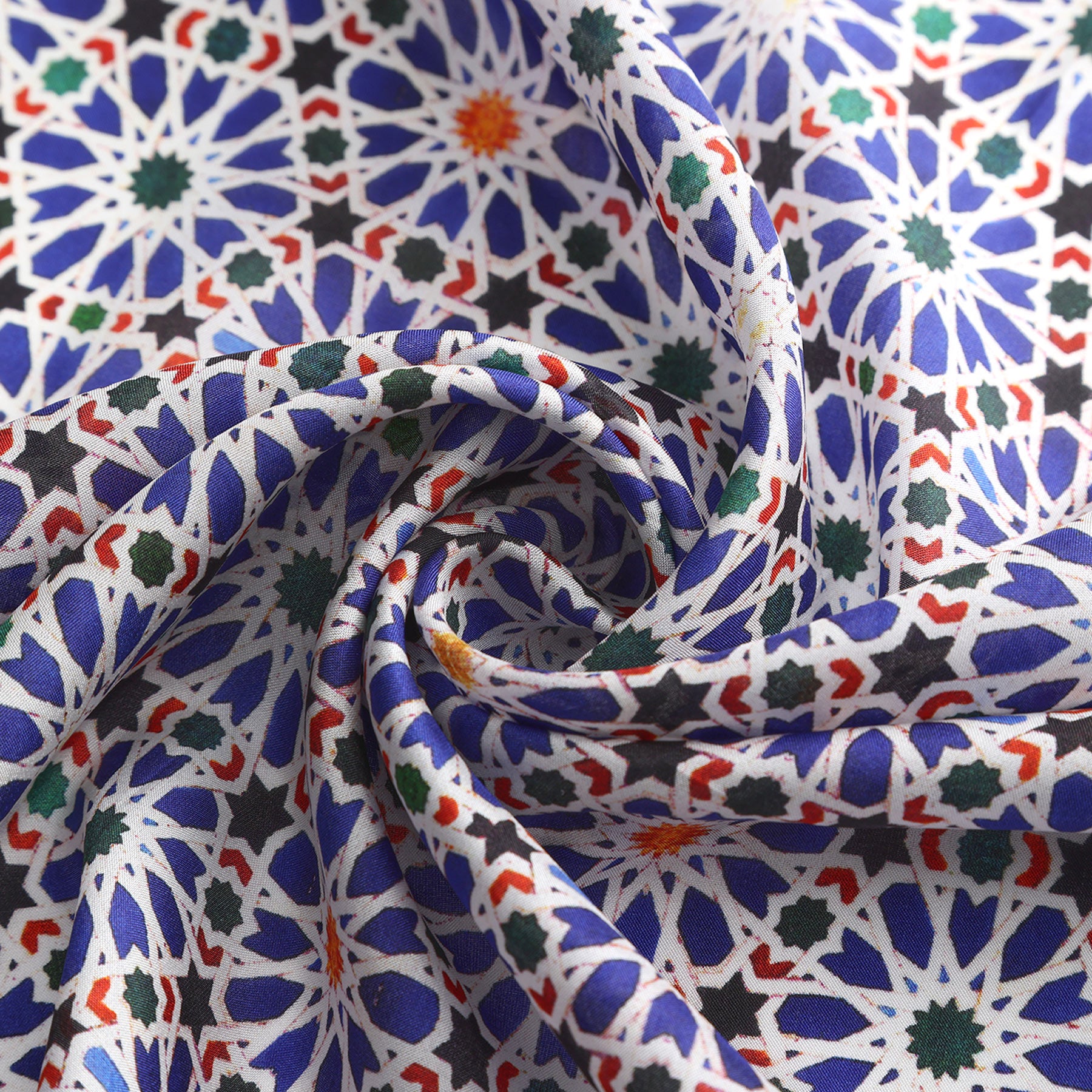 A close-up of the Blue Square Scarf Zellige v2 shows its vibrant geometric mosaic pattern inspired by Islamic art, arranged in a spiral fold with intricate star and floral motifs in blue, white, orange, green, and black.