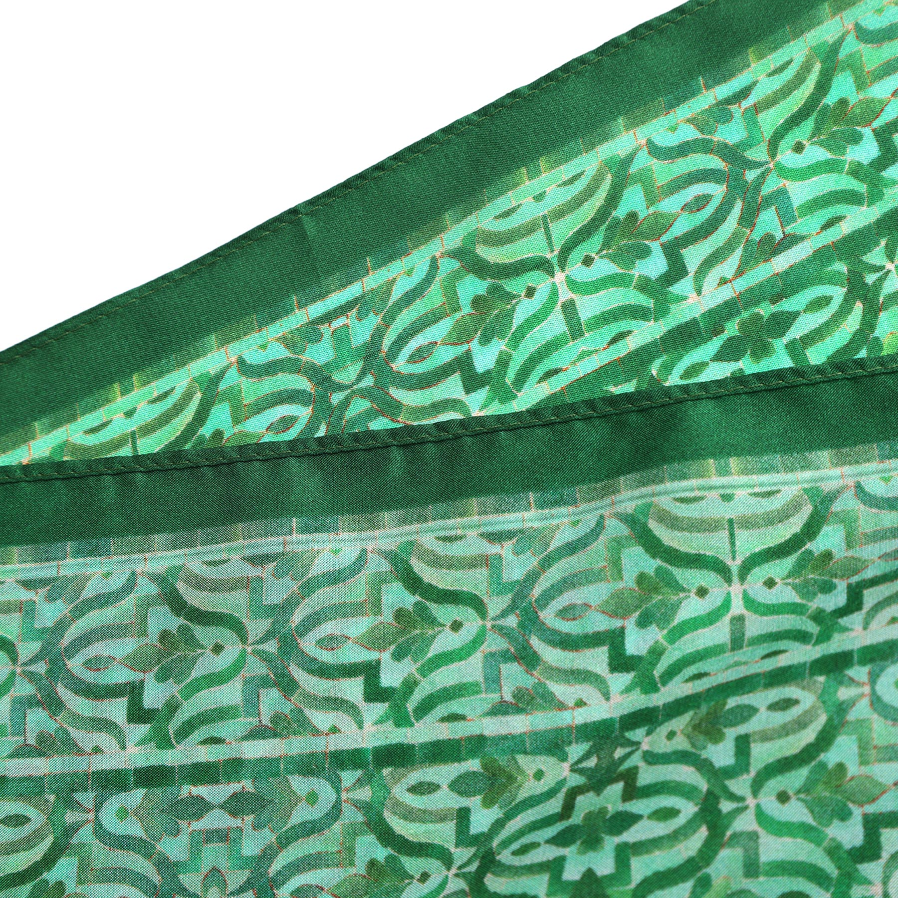 A close-up of the Green Square Silk Scarf Fihri shows intricate geometric and floral patterns inspired by Alhambra Palace, with light and dark green shades and visible edge stitching.