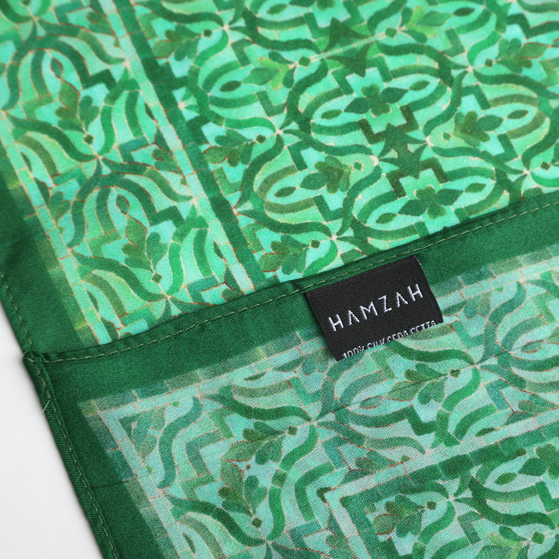 A close-up of the Green Square Silk Scarf Fihri, featuring a green geometric floral pattern inspired by Islamic art and a black HAMZAH label in white text.