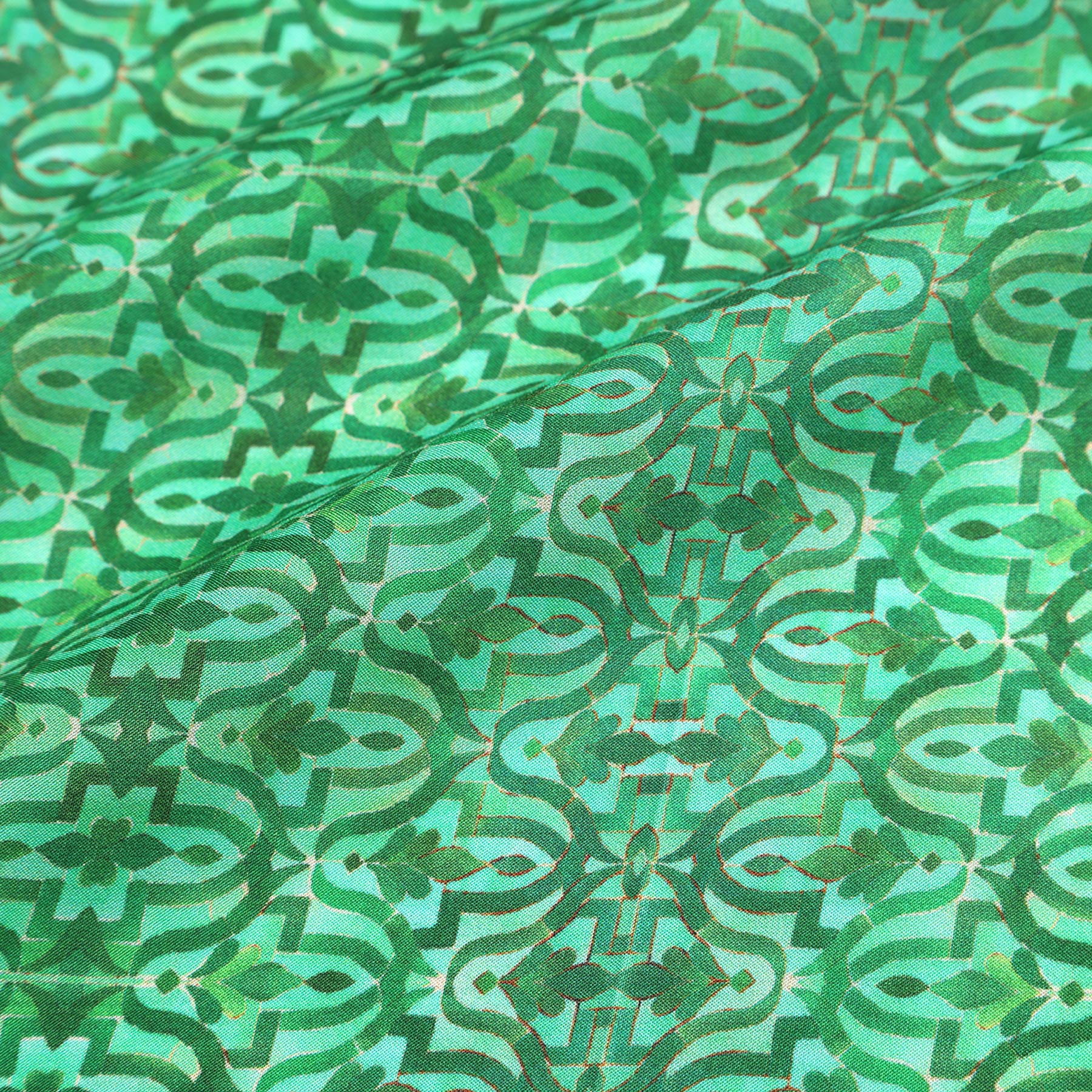 Close-up of the Green Square Silk Scarf Fihri, showcasing an intricate geometric and floral pattern inspired by Alhambra Palace Islamic art, with gold accents enhancing its vibrant green silk and textured appearance. The fabric is gently folded.