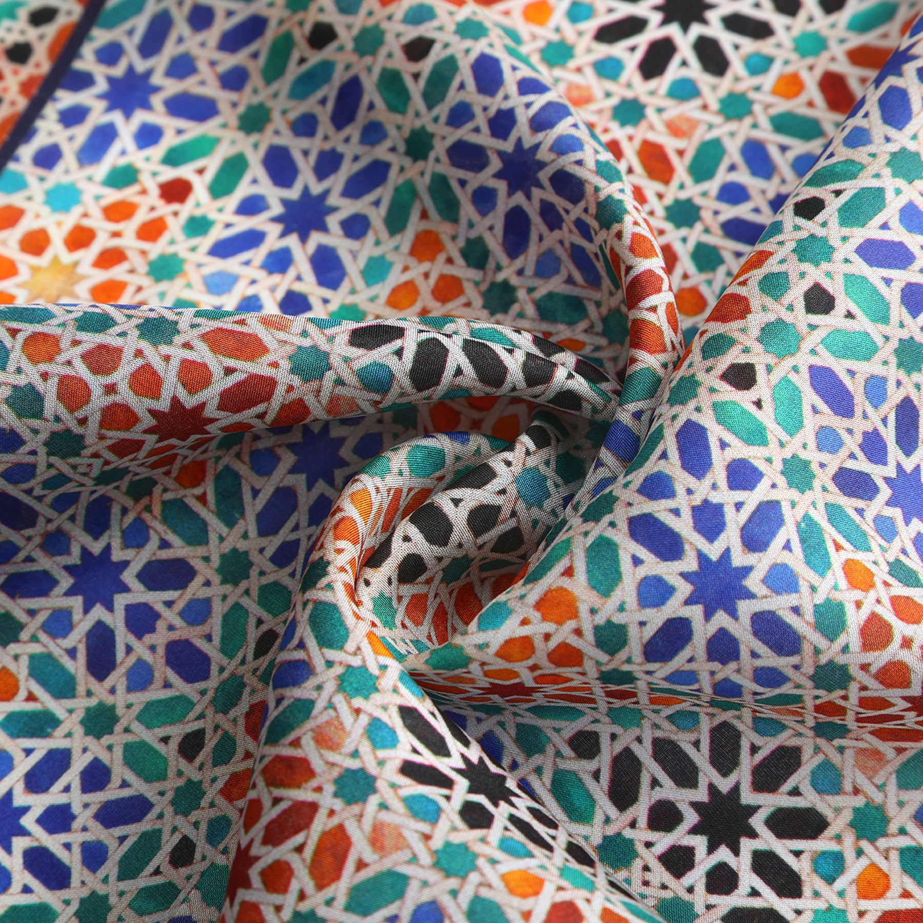 A close-up of the Square Scarf Blue Madiya, a silk piece with intricate Islamic geometric patterns in blue, orange, black, and green, draped in soft folds for added texture and depth.