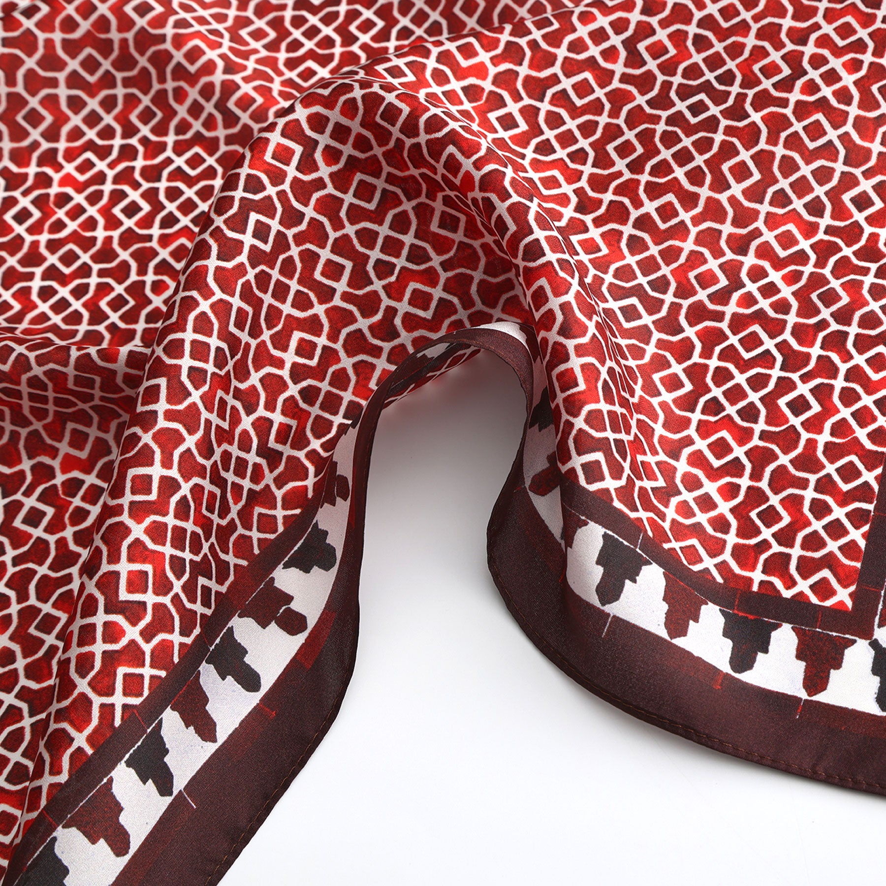 The Red Square Scarf 100% Silk features red and white geometric patterns inspired by Islamic art, a dark border with small silhouettes, and is displayed draped on a flat white surface.