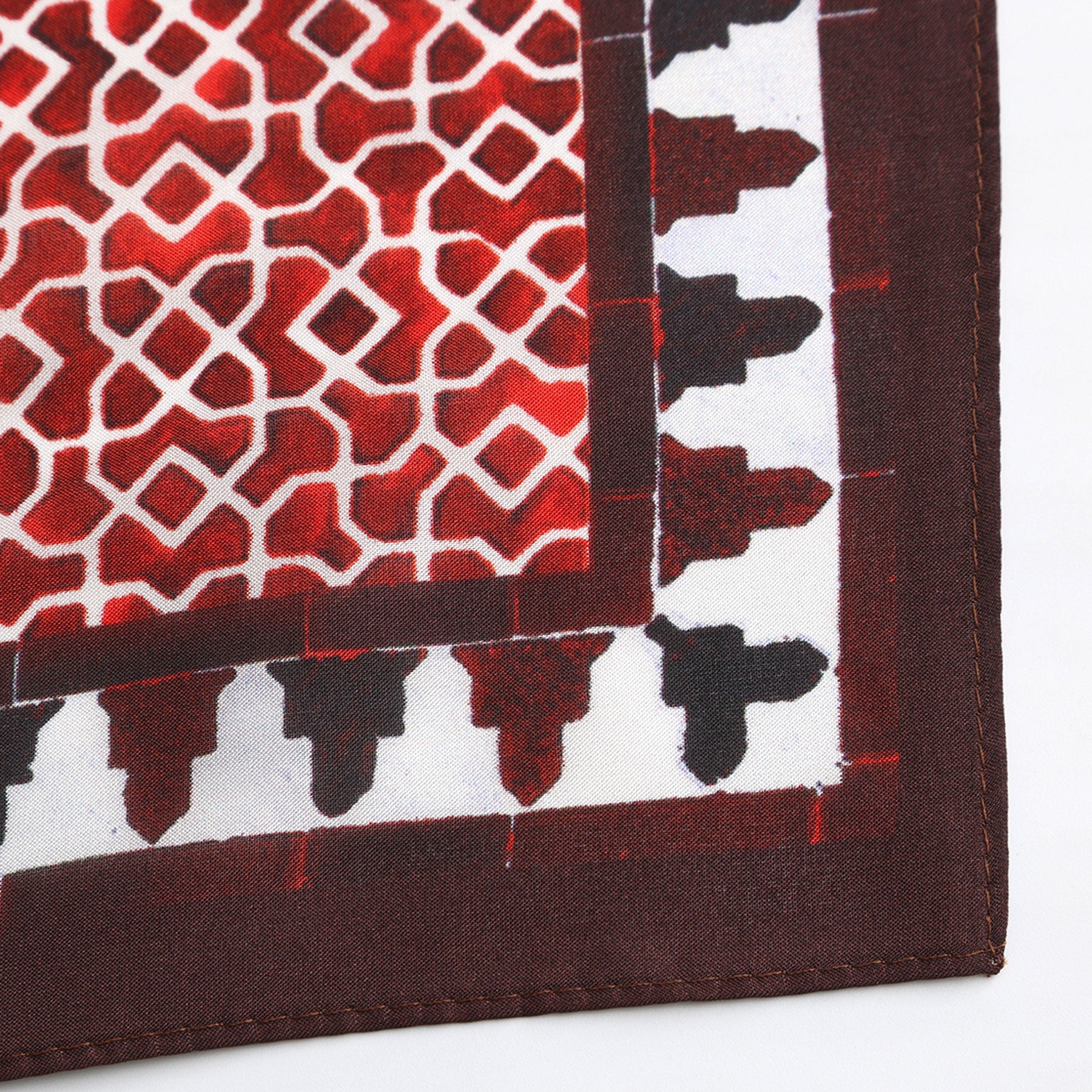 Close-up of the Red Square Scarf 100% Silk, showcasing its geometric red, white, and black diamond patterns and stitched brown edges, inspired by Alhambra Palace motifs.