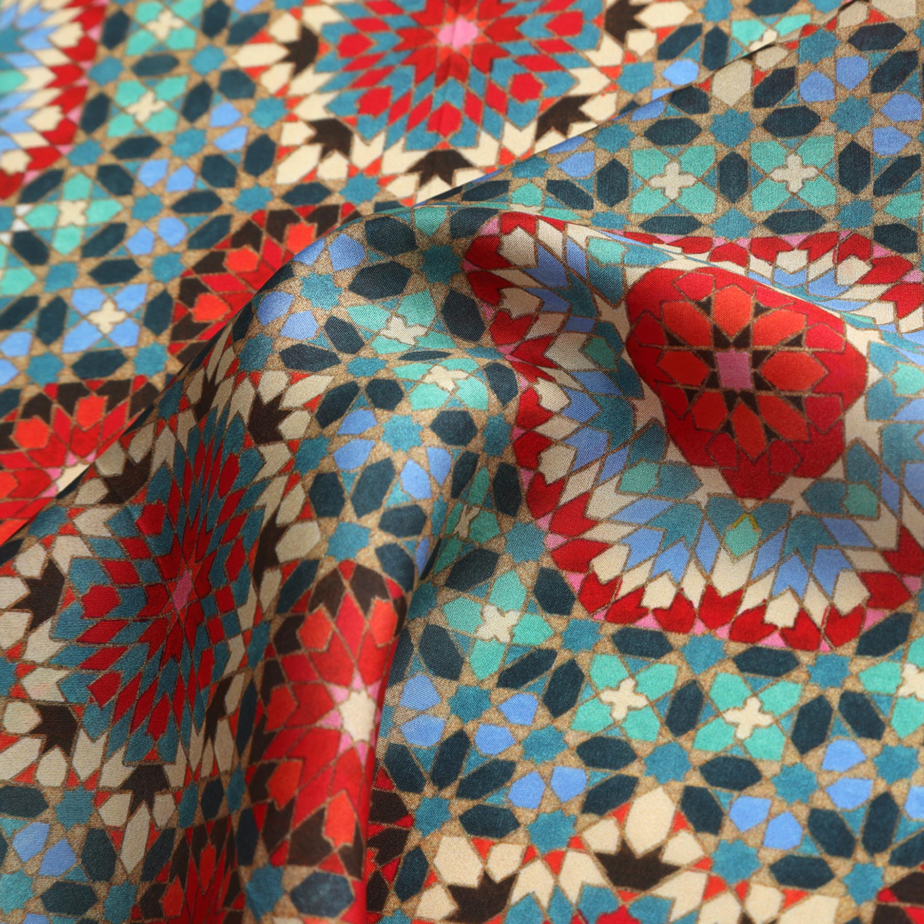 A close-up of the Colorful Silk Neckerchief, showcasing its geometric, mosaic-inspired Islamic art print in red, blue, teal, and brown starburst shapes. The silk fabric is gently draped to reveal its smooth texture and flowing folds.
