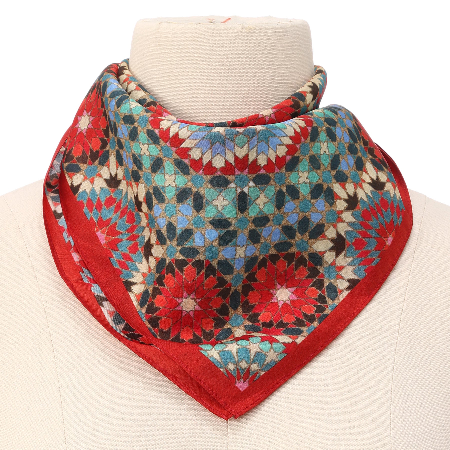A mannequin displays the Colorful Silk Neckerchief, featuring an Islamic art-inspired geometric mosaic pattern in blue, red, black, and white with a solid red border. The silk scarf is elegantly folded and draped around the neck.