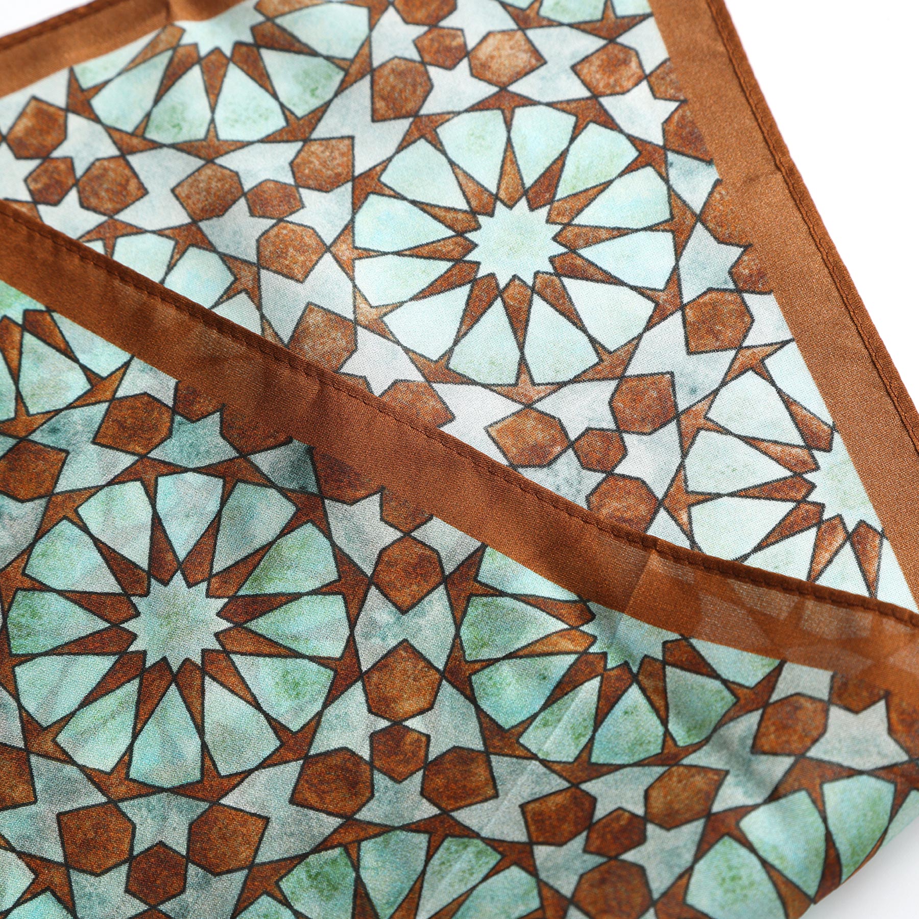 A close-up of the Brown Silk Neckerchief for Women, folded to display its geometric pattern in light blue and white, featuring intersecting stars and polygons inspired by traditional Islamic art and Spanish craftsmanship.