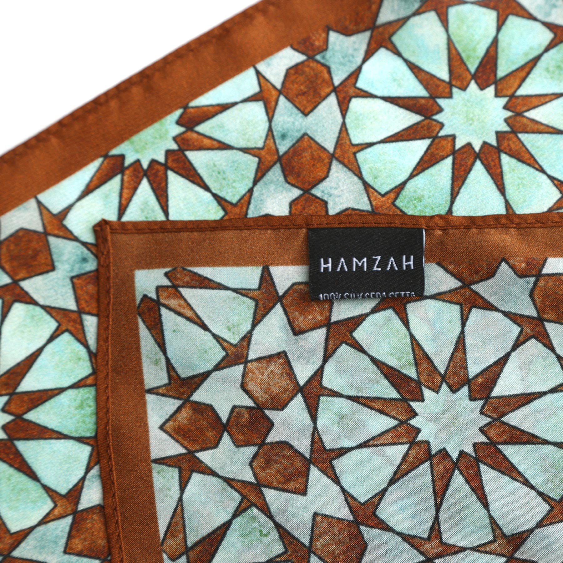 Close-up of the Brown Silk Neckerchief for Women featuring a turquoise and white geometric star pattern inspired by Islamic art, a black HAMZAH label at the edge, and refined Spanish craftsmanship.