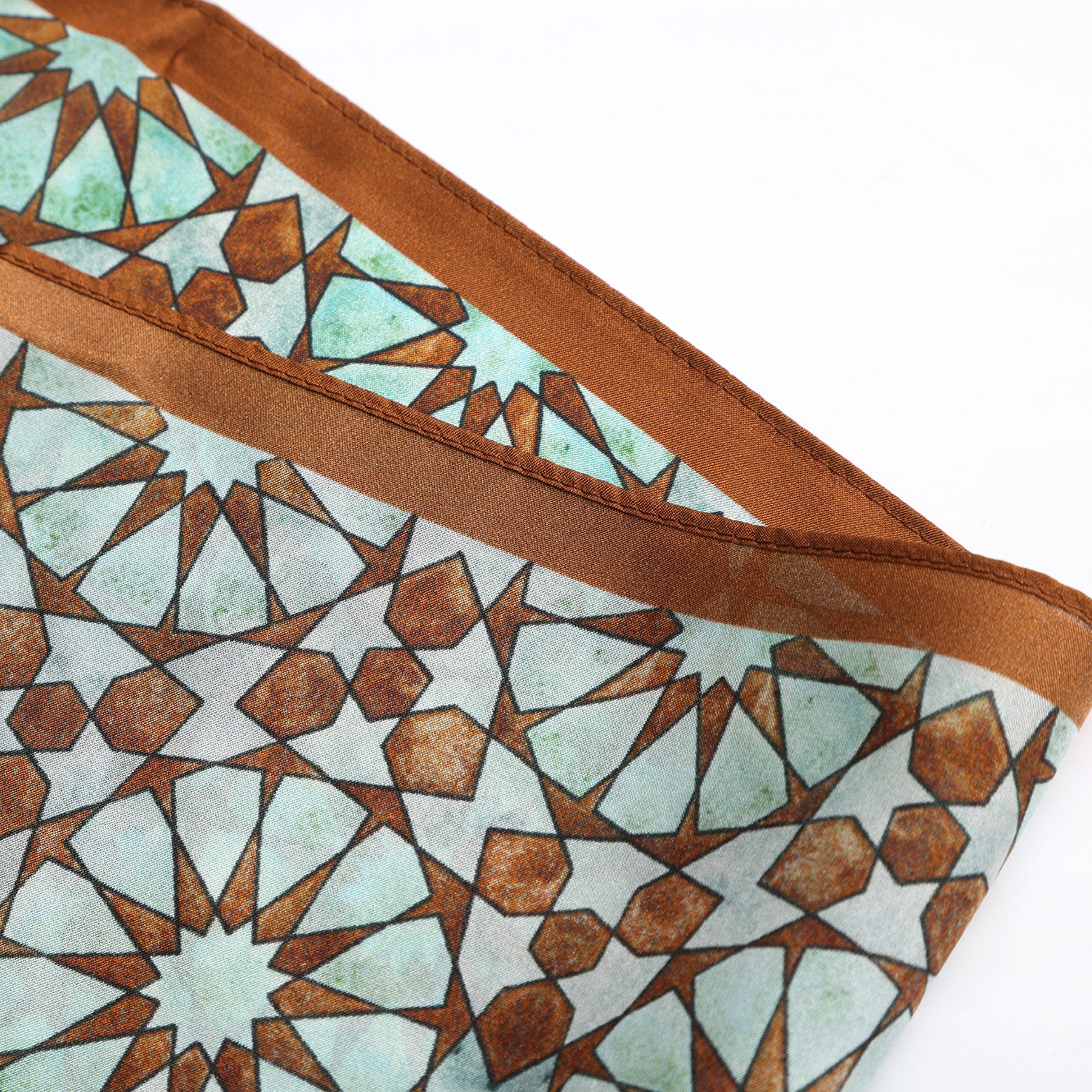 The Brown Silk Neckerchief for Women is shown folded on a white background, featuring a geometric star pattern inspired by Islamic art in brown and turquoise, bordered with a solid brown edge.