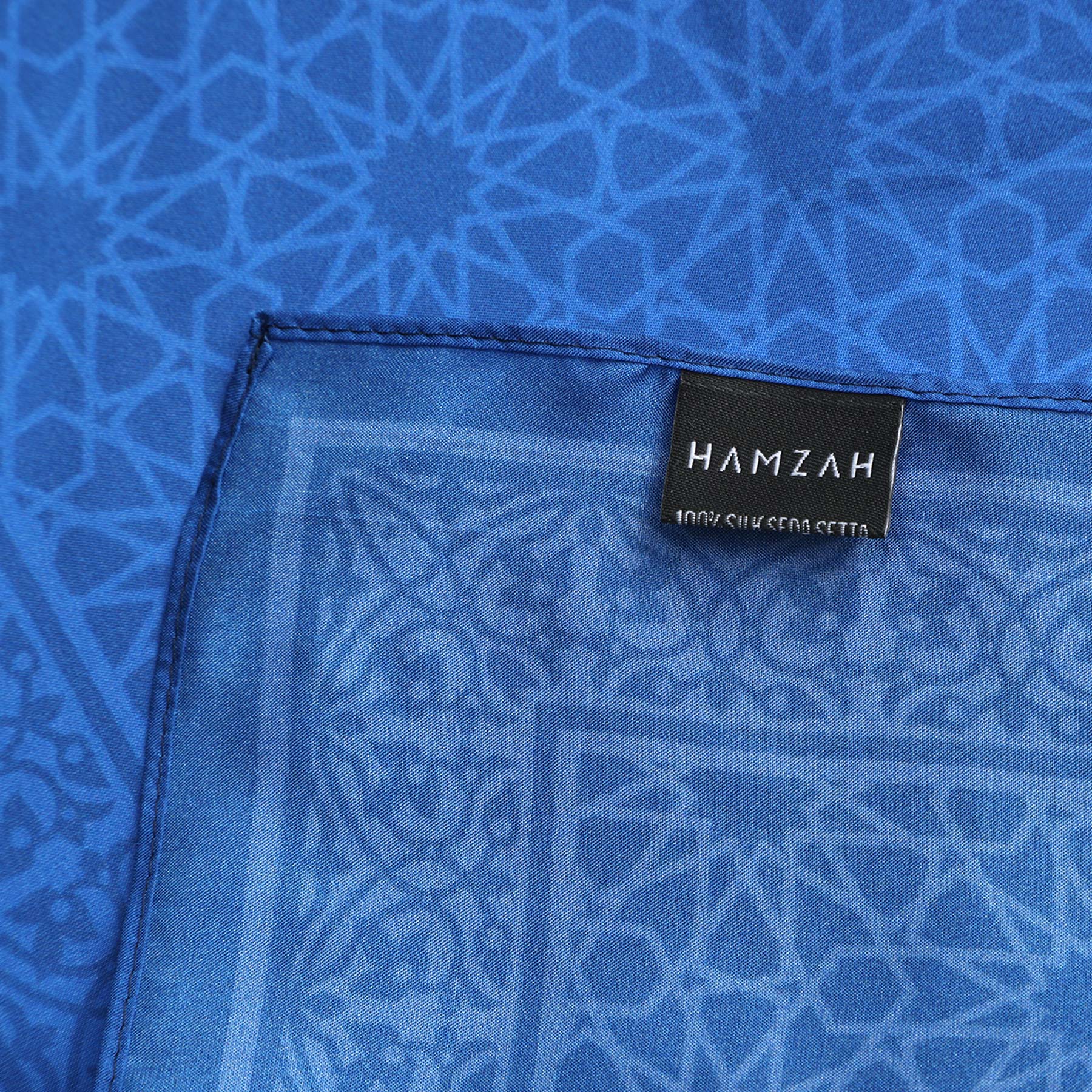 A close-up of the Blue Square Silk Scarf Dalila v1, featuring intricate Alhambra-inspired geometric patterns and a label sewn on one edge.