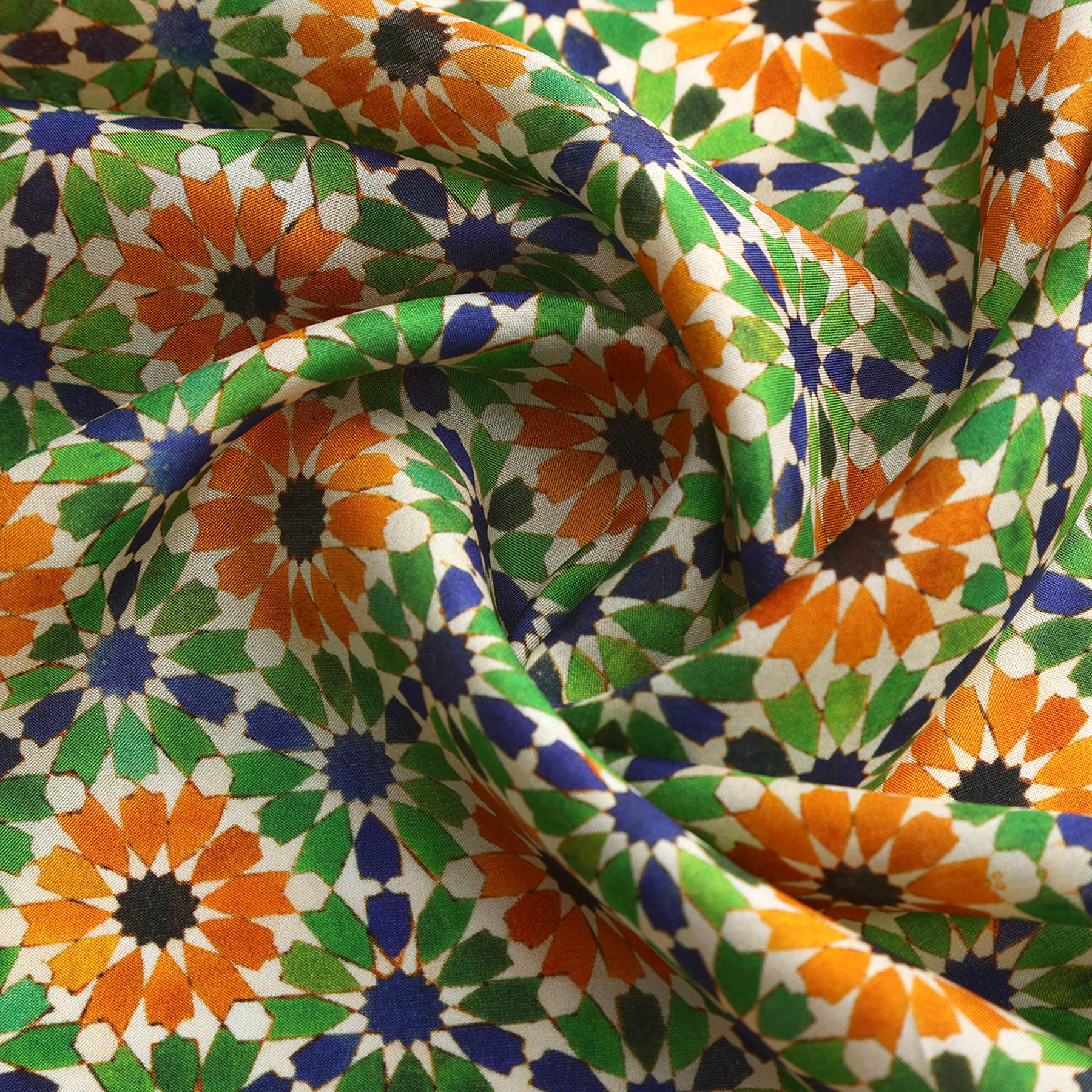 A close-up of the Islamic Art Print Square Silk Scarf Nur, showcasing a vibrant geometric mosaic with star motifs in green, orange, blue, black, and white. The softly folded silk creates gentle shadows and highlights its refined texture.