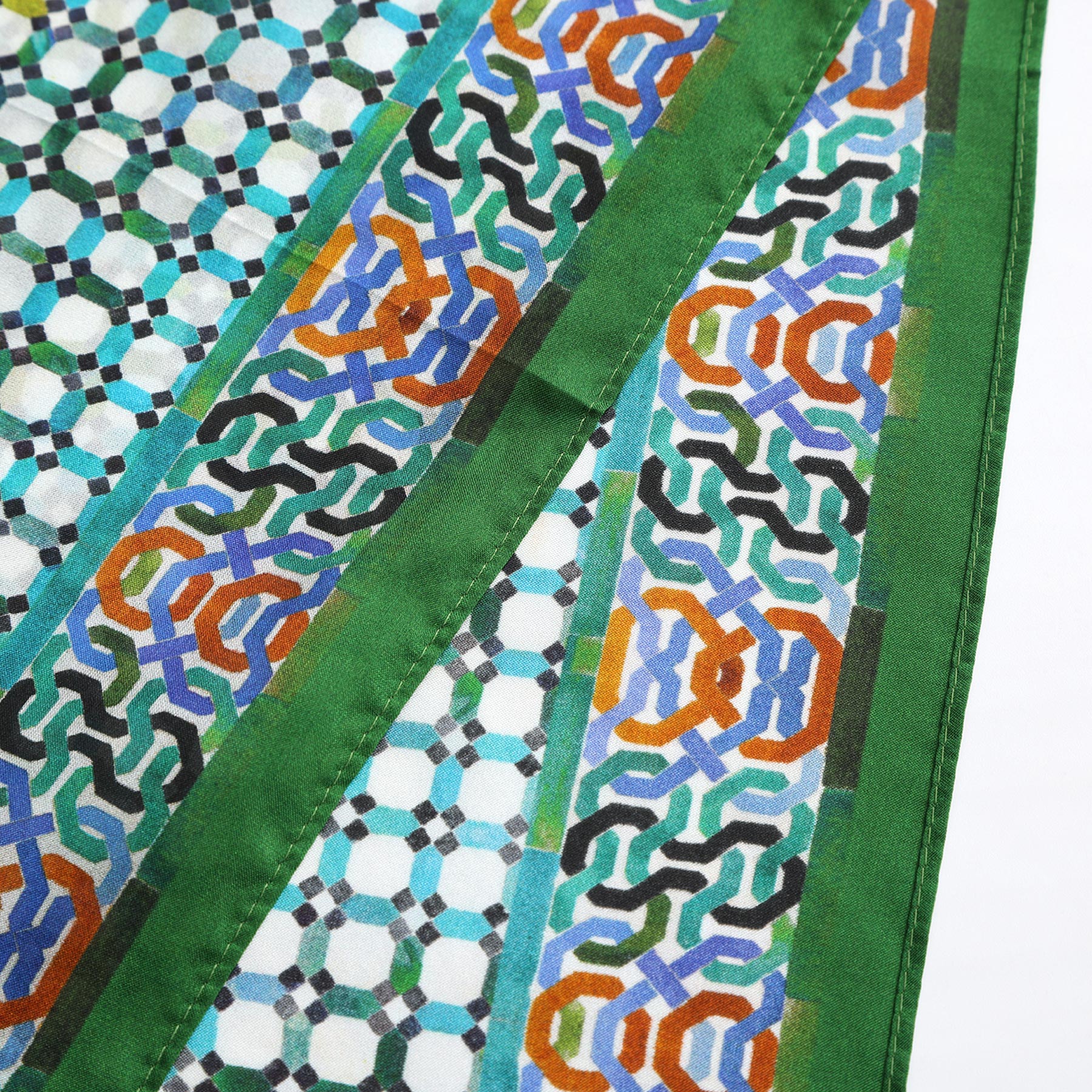 A close-up of the Coloful Neckerchief 100% Silk, showcasing intricate Alhambra-inspired geometric patterns in green, blue, orange, and black with solid green borders on a white background.