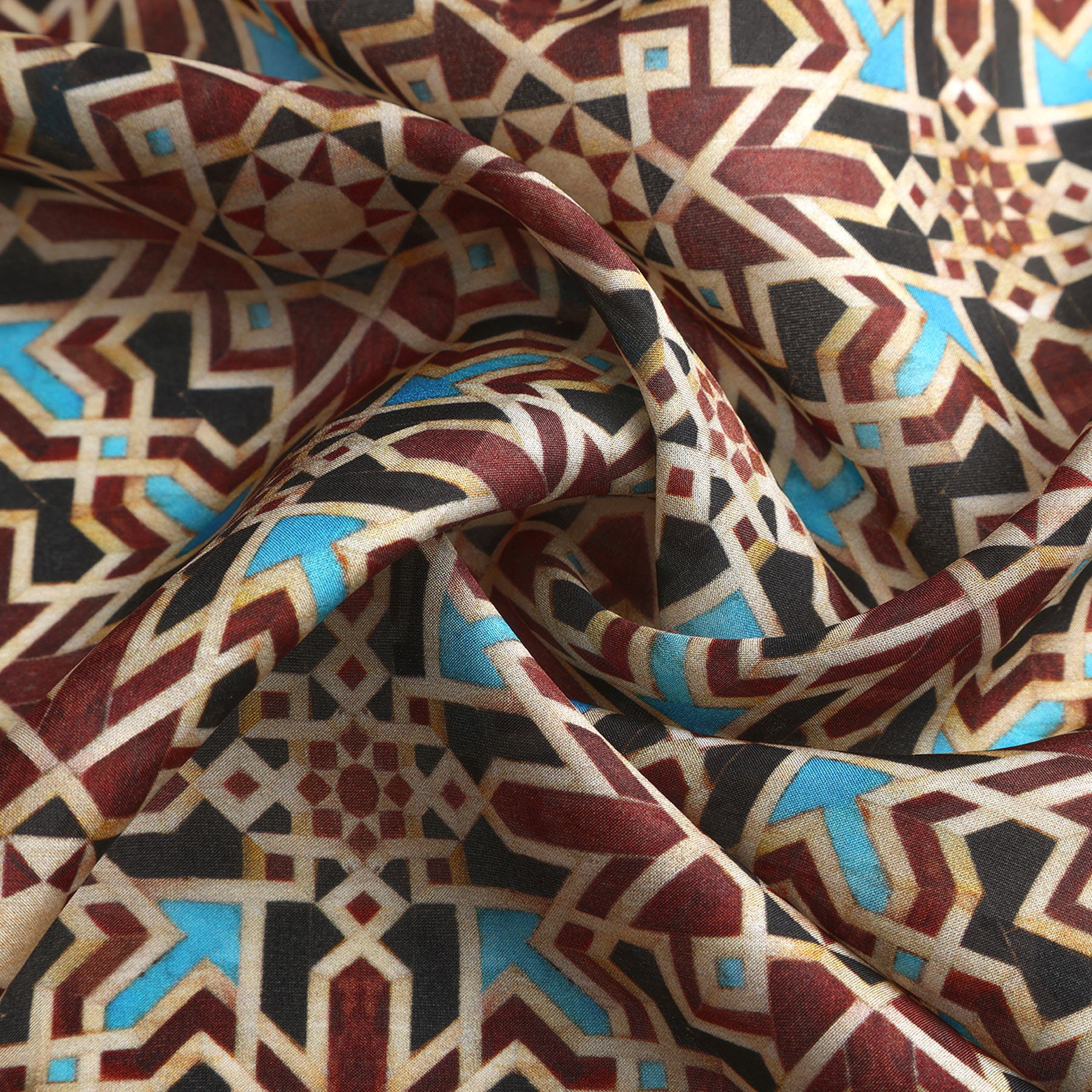 A close-up of the Brown Silk Neckerchief shows its intricate geometric pattern in red, brown, beige, blue, and black. The softly draped silk highlights Islamic art-inspired details and hints at Spanish craftsmanship.